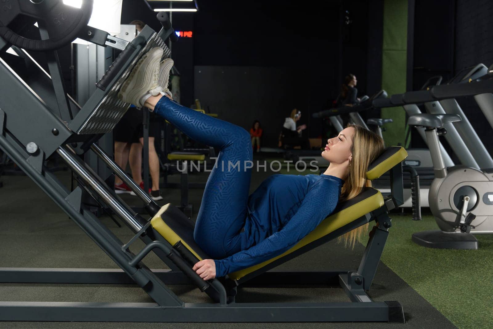 Young woman working her quads at machine press in the gym. wearing blue leggins and long sleeve top.