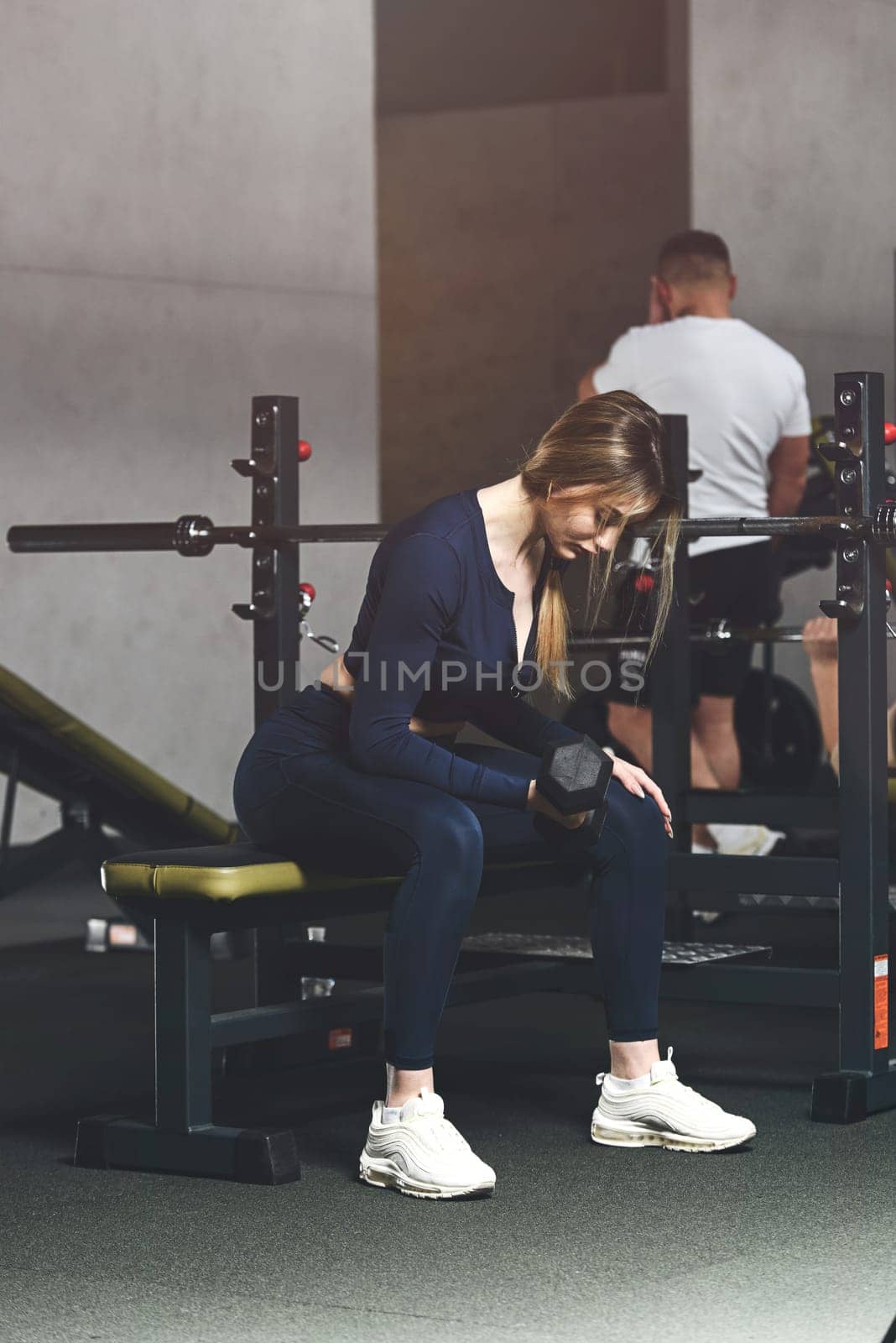 Woman doing biceps curl with dumbbells in seated position. white sneakers