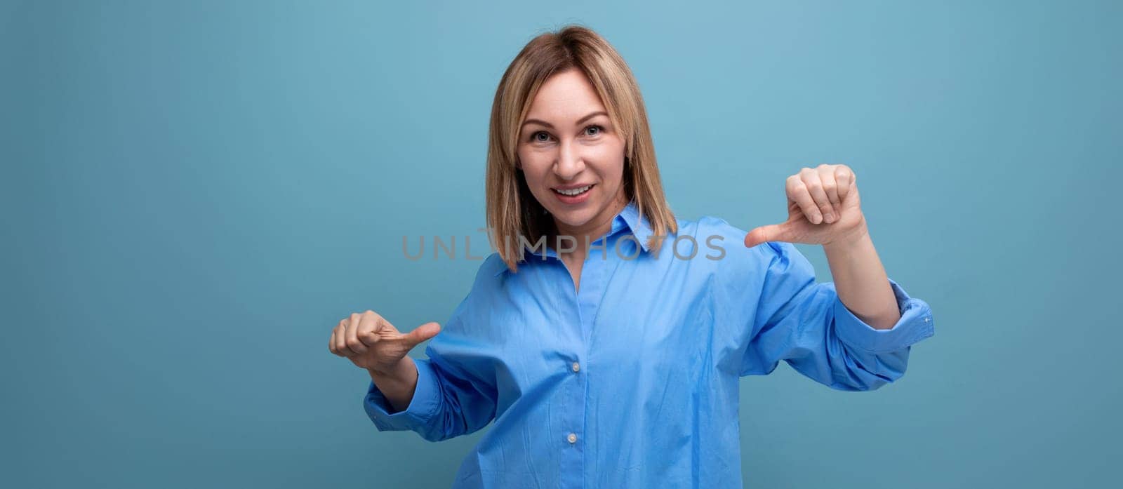 confident blond young millennial in casual shirt shows hands super at herself on blue background with copy space by TRMK