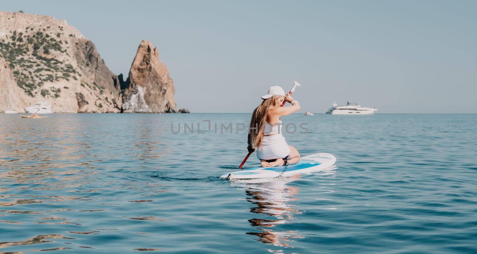 Close up shot of beautiful young caucasian woman with black hair and freckles looking at camera and smiling. Cute woman portrait in a pink bikini posing on a volcanic rock high above the sea