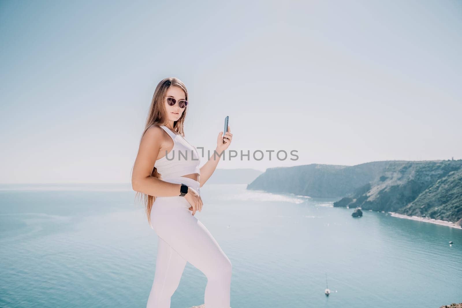 Digital nomad, woman in the hat, a business woman with a laptop sits on the rocks by the sea during sunset, makes a business transaction online from a distance. Freelance, remote work on vacation. by panophotograph