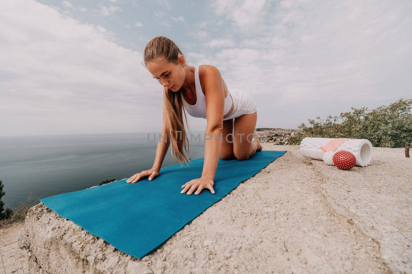 Woman sea pilates. Sporty, middle-aged woman practicing pilates in park near the sea. trains on a yoga mat and exudes a happy and active demeanor. healthy lifestyle through exercise and meditation. by panophotograph