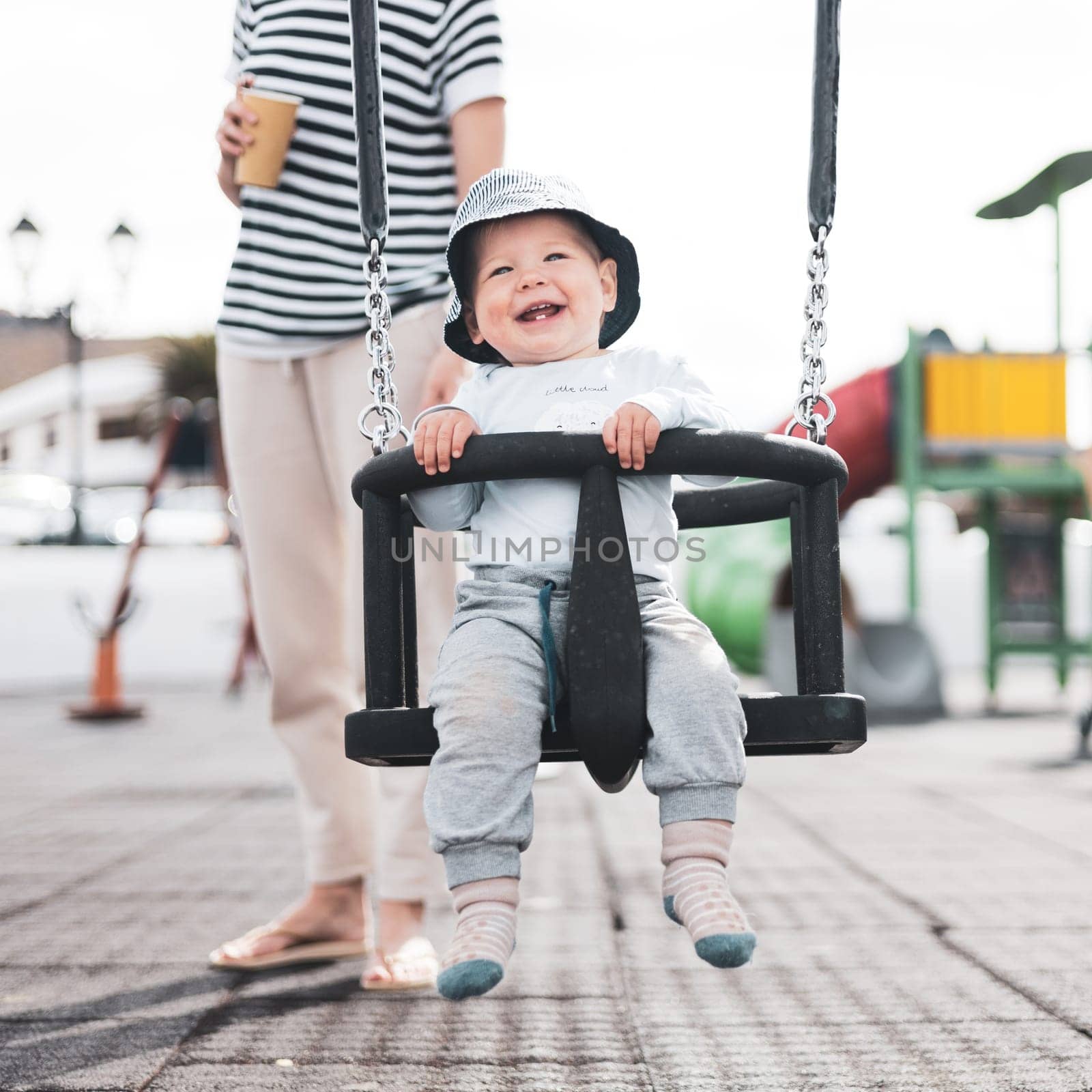 Mother pushing her infant baby boy child on a swing on playground outdoors. by kasto