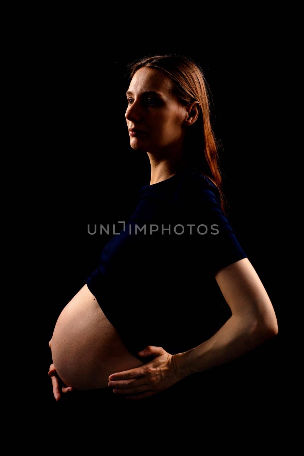 Beautiful pregnant woman over black background. Artistic low key light in studio. High quality photo