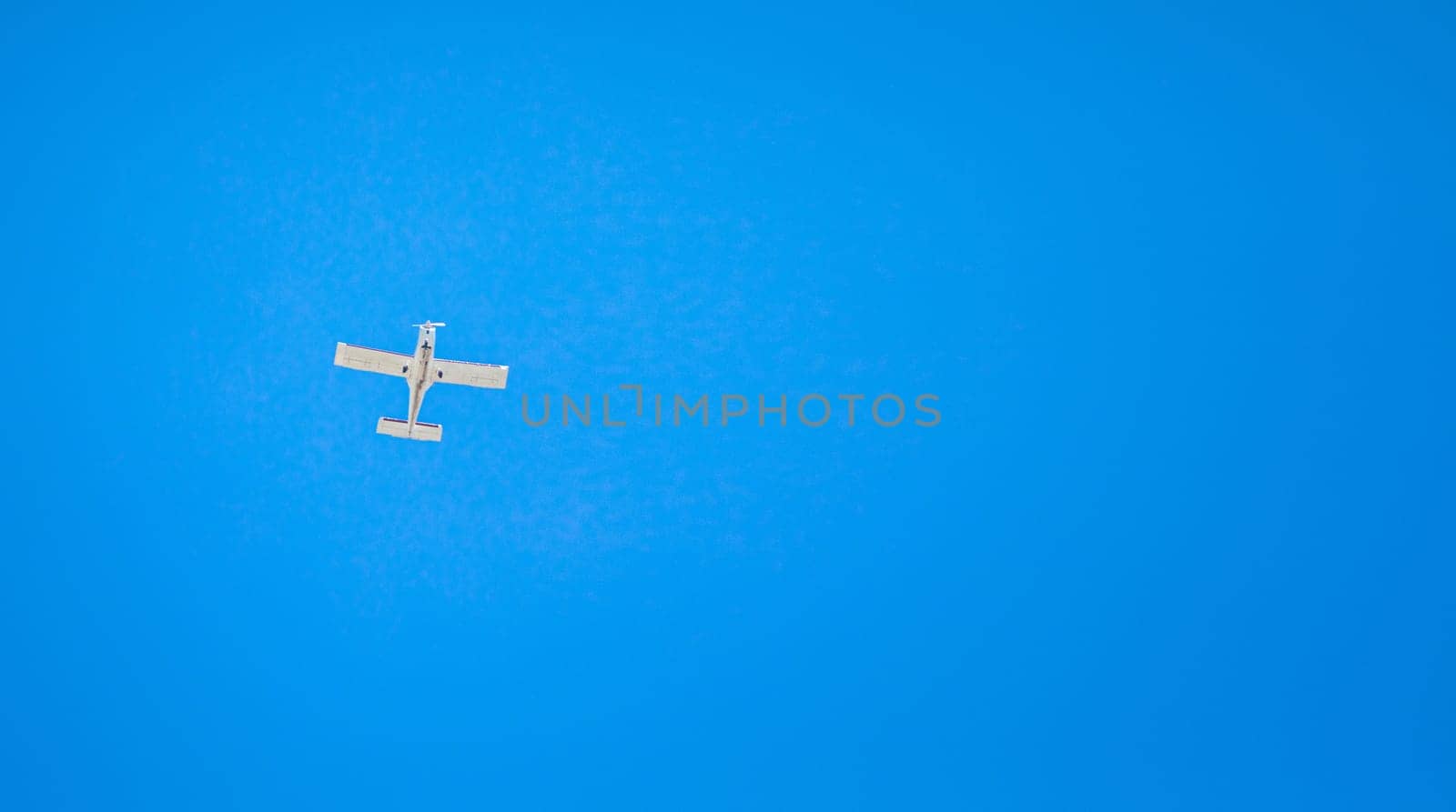 A small light plane flies in the clear sky. View from below. Horizontal orientation