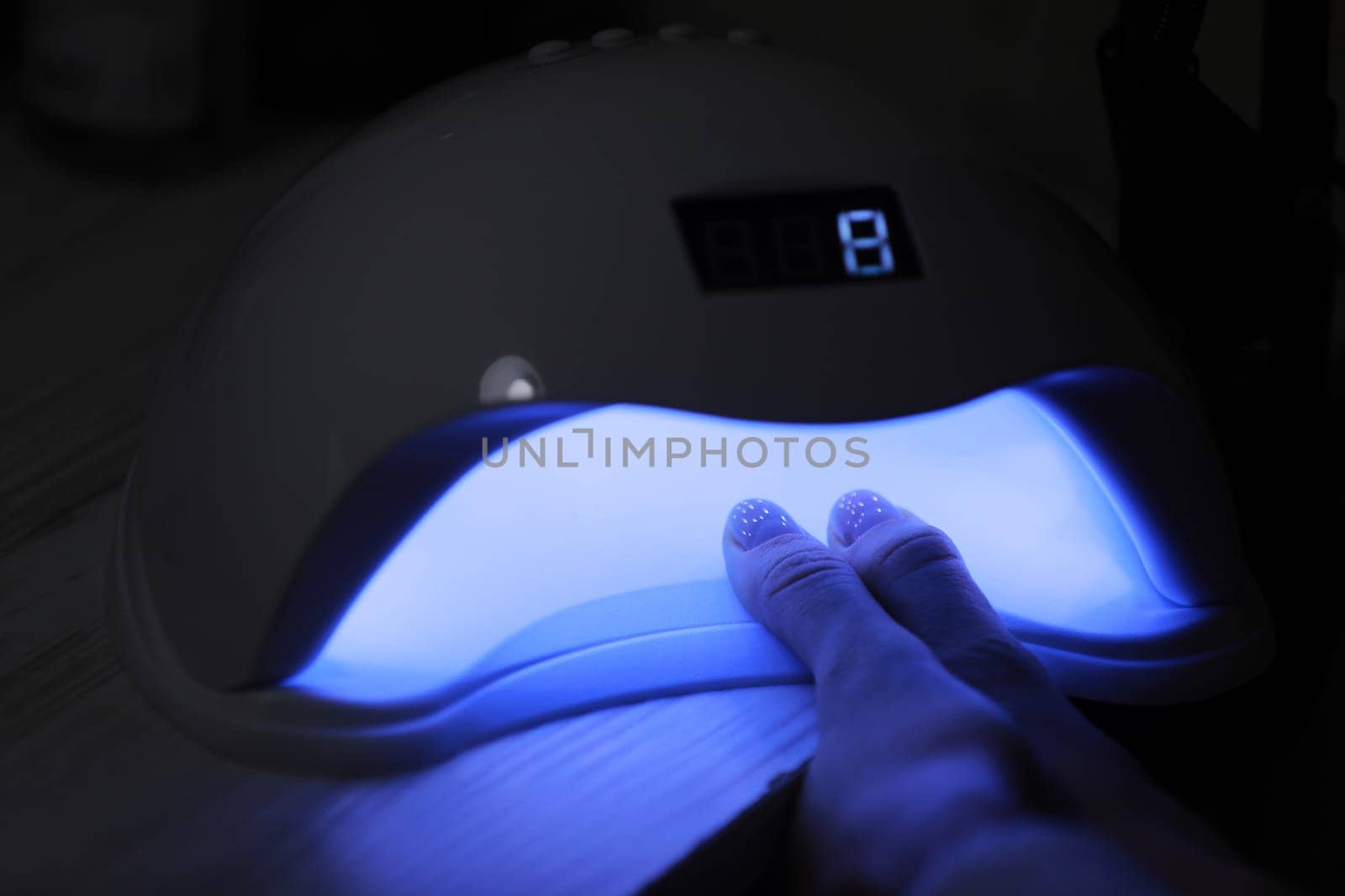 Closeup view of female hands with gel polish manicure. Woman puts hand into led uv lamp for curing top cover of nailpolish. UV lamp, LED Nail. by Andriimedvediuk