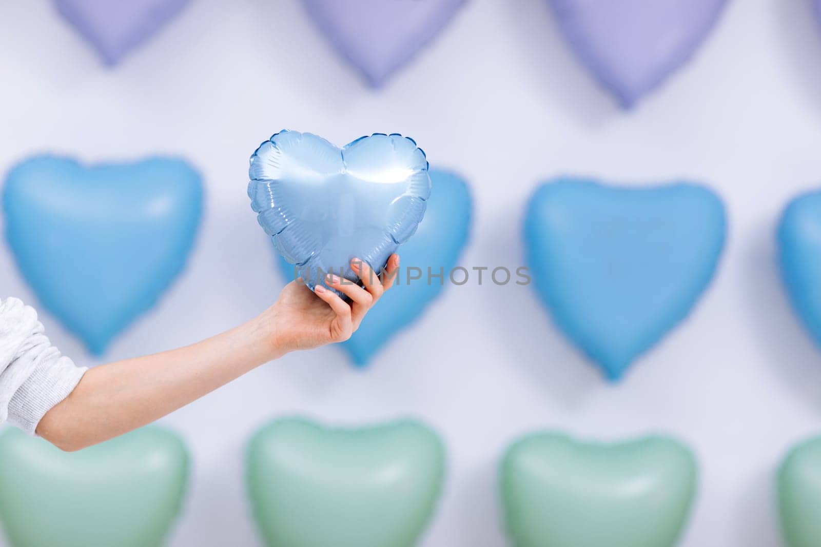 The woman holds the blue balloon in the form of a heart on many hearts background. valentines day. selective focus.