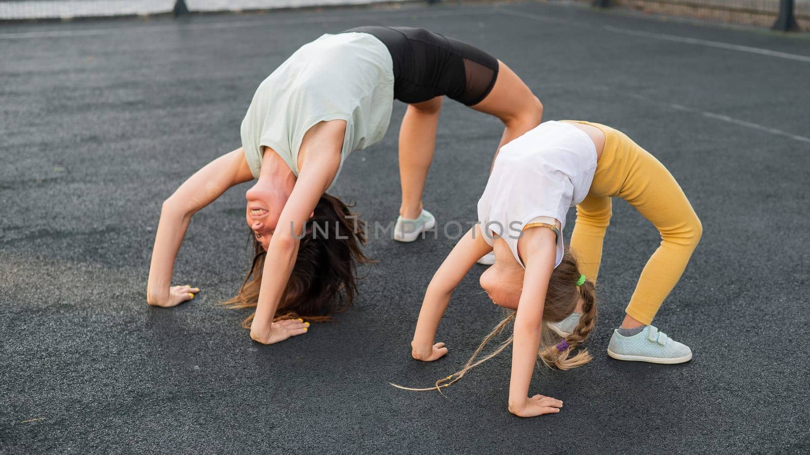 A little girl and her mom do a bridge exercise at the outdoor sports ground