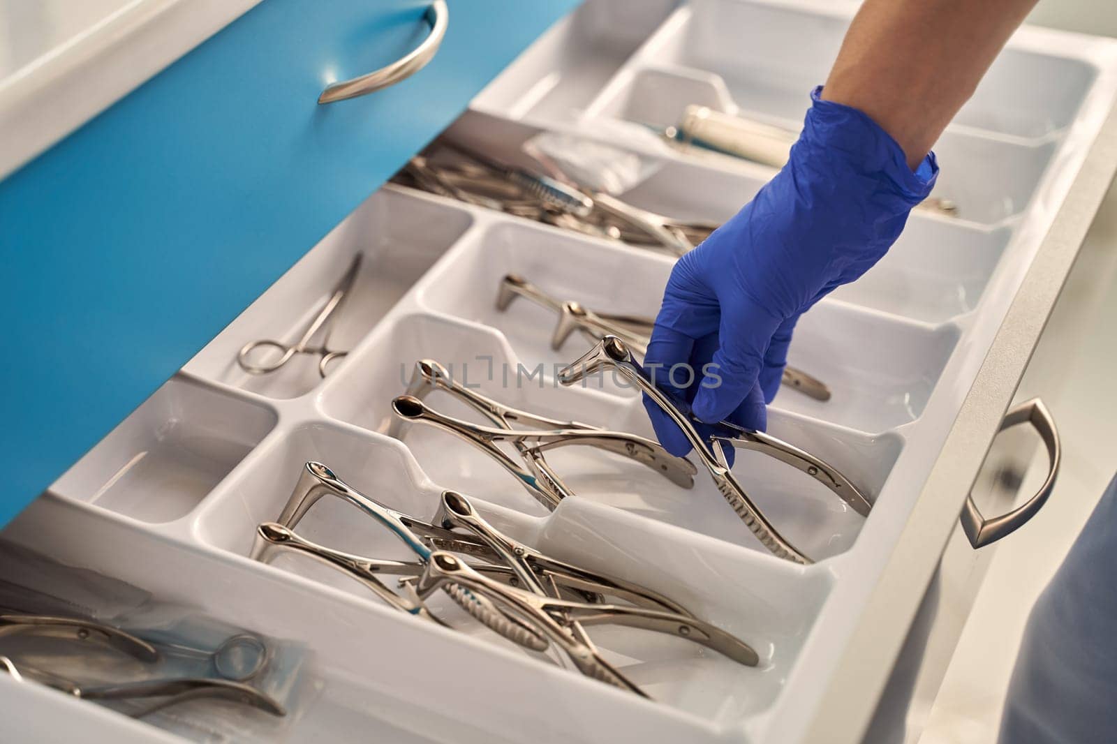 Doctor's hand wearing a disposable medical gloves holding a stainless steel nasal speculum for ENT examination over other surgery instruments