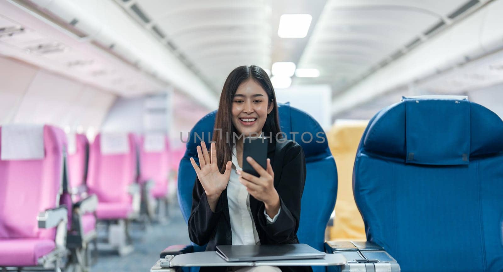 Asian female using mobile phone with talking and Video calls in airplane, Business traveling and technology concept by nateemee