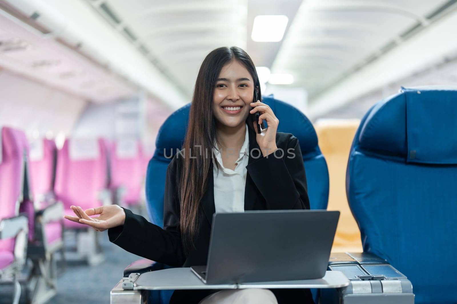 attractive businessman in suit with talking on mobile phone and working on laptop while sitting in airplane cabin. Work and travel concept.