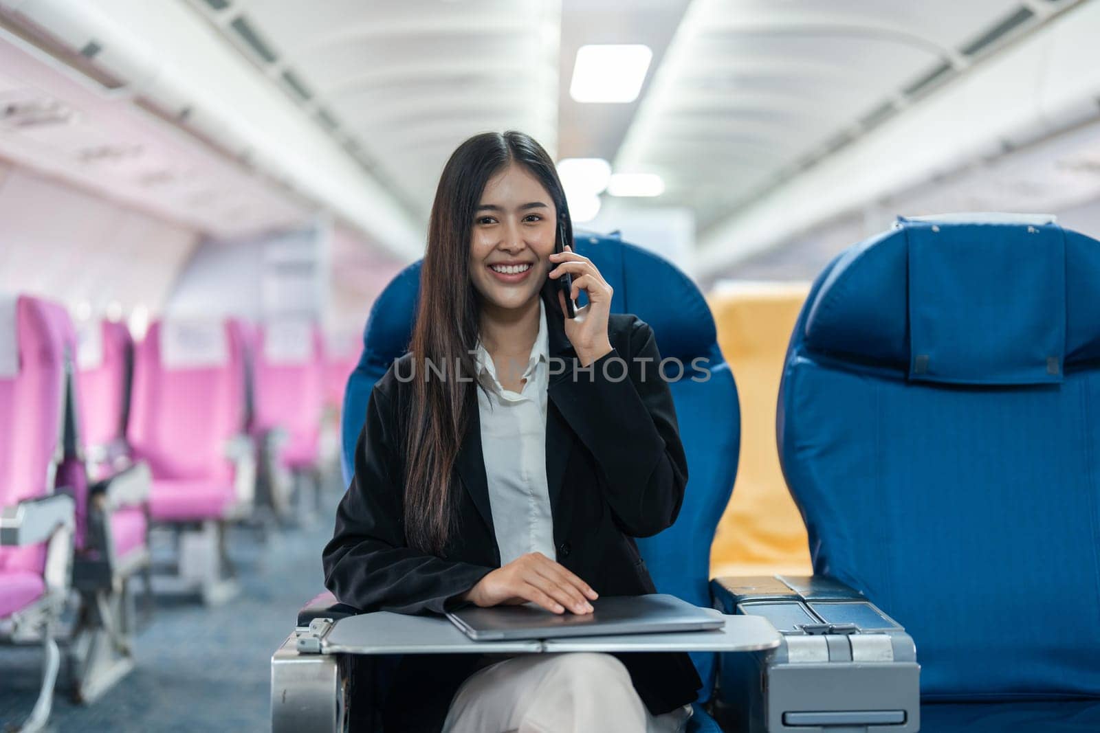 attractive businessman in suit with talking on mobile phone and working on laptop while sitting in airplane cabin. Work and travel concept.