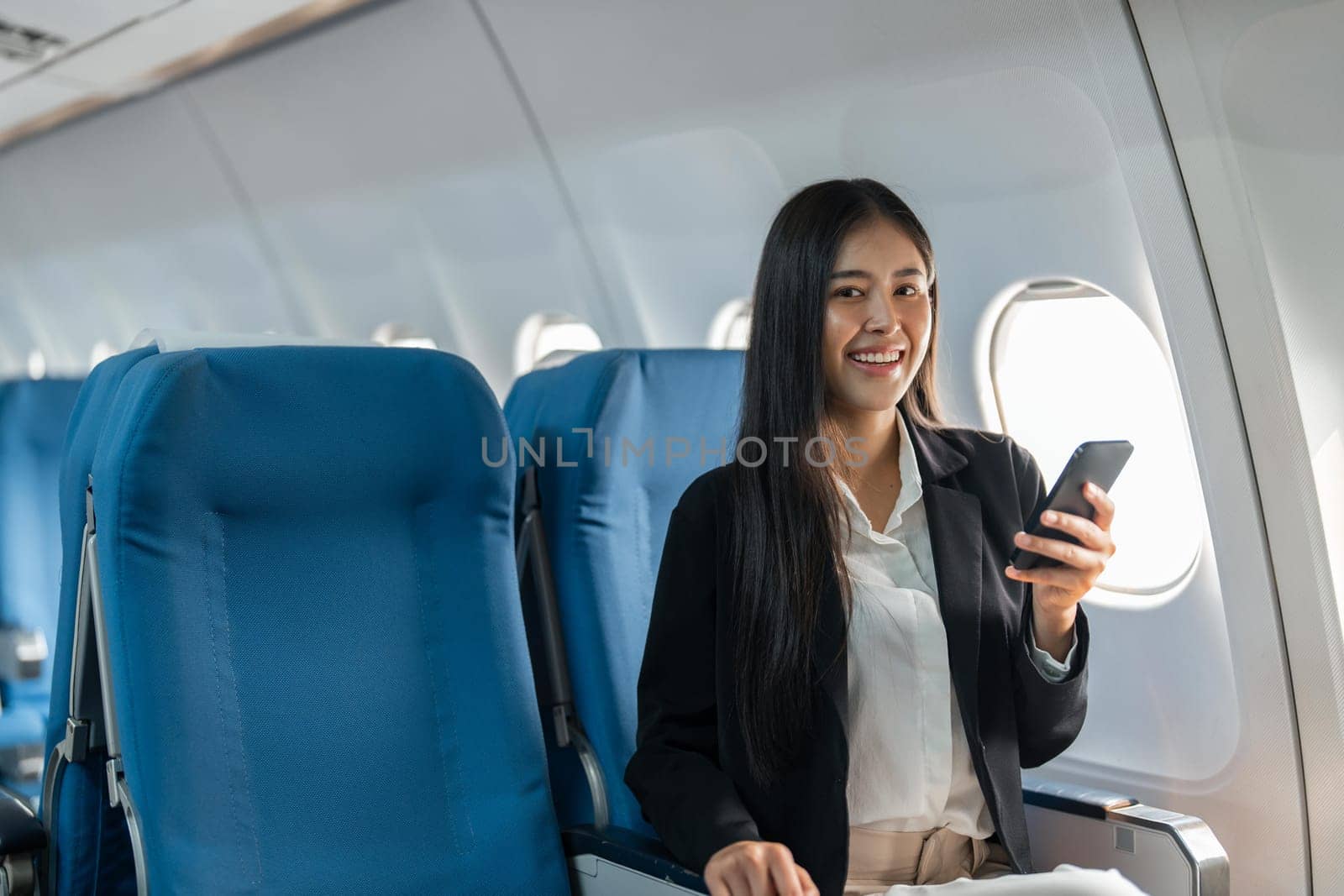 female traveler passenger sits at the window seat in economy class, using his smartphone.