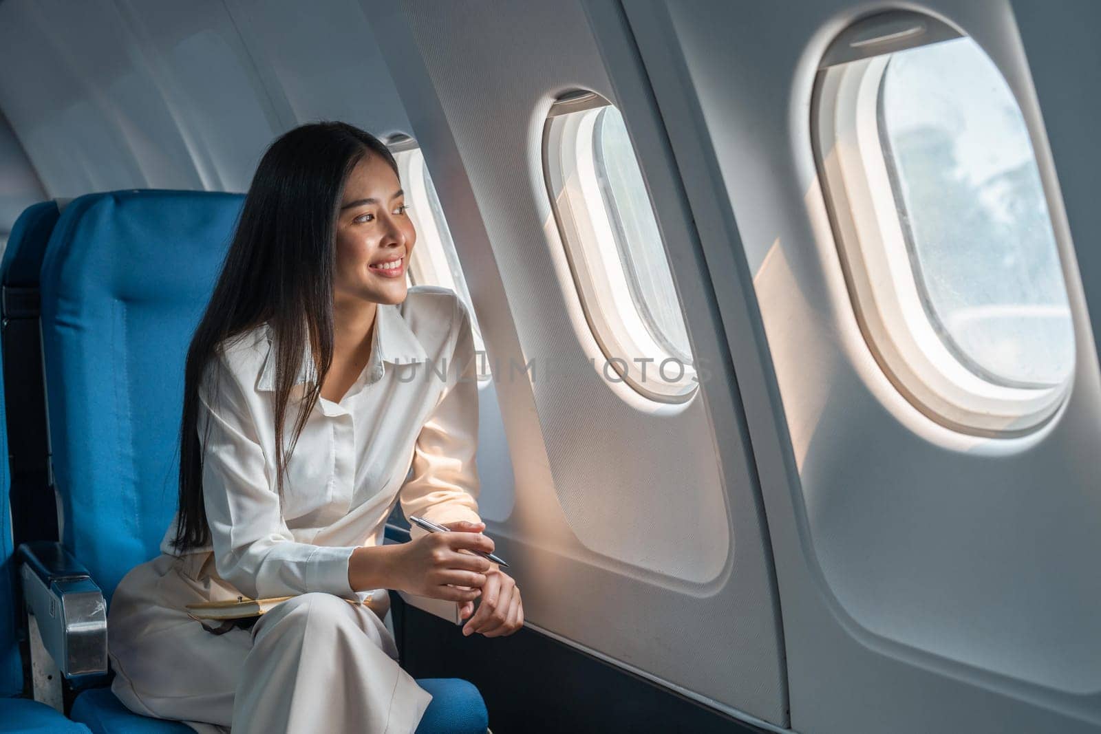 Asian woman sitting in a seat in airplane and looking out the window going on a trip vacation travel concept.