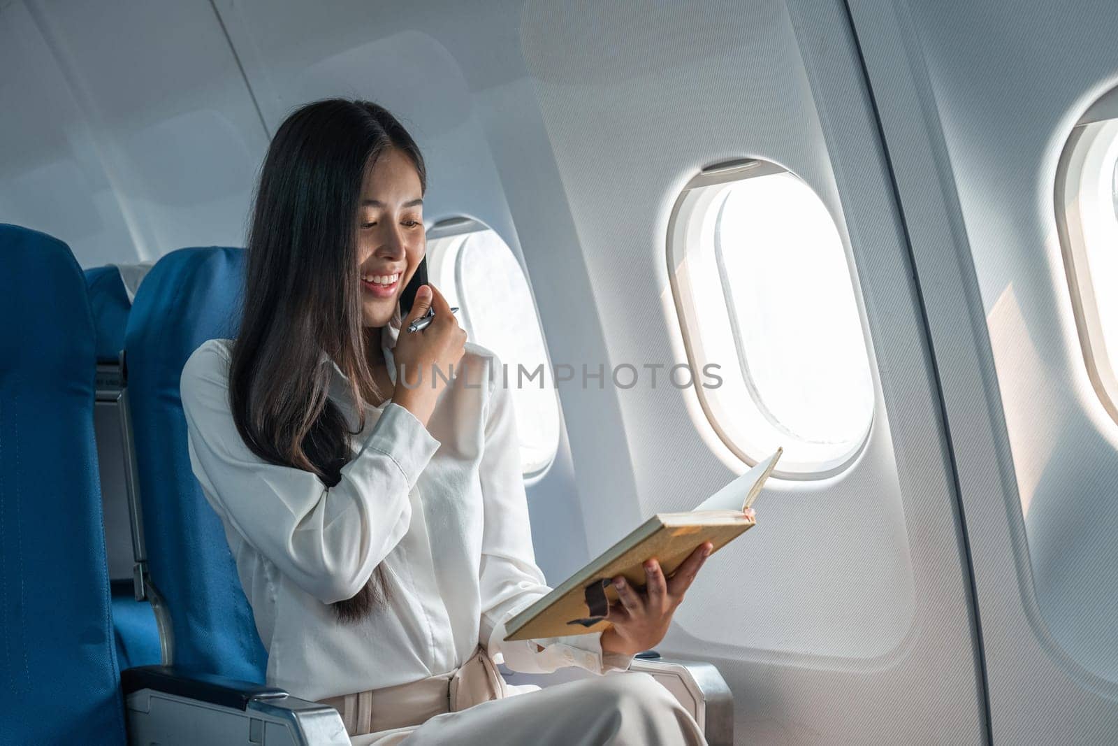 Business young asian woman talking on phone during for data financial report on airplane.