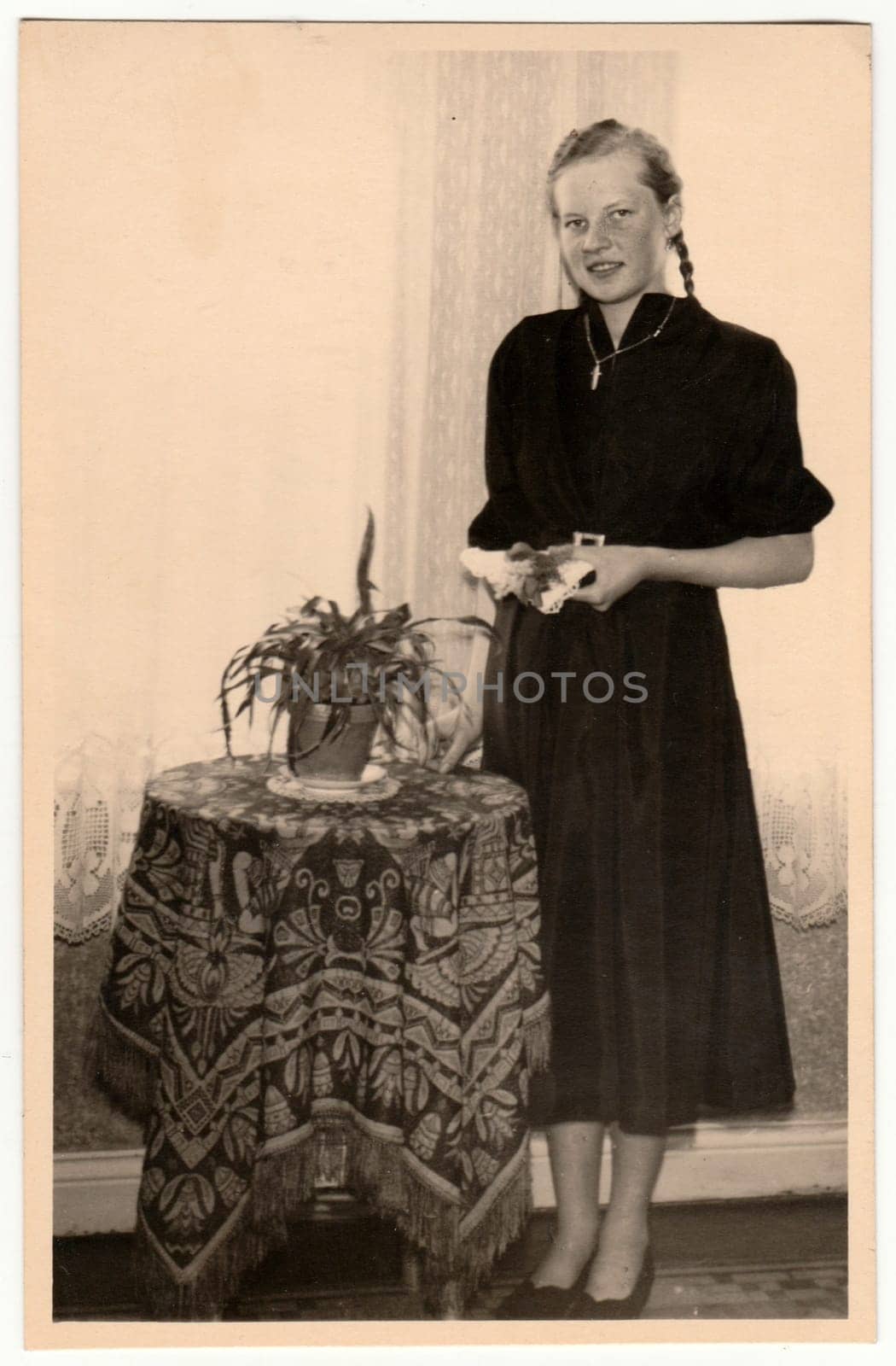 THE CZECHOSLOVAK SOCIALIST REPUBLIC - CIRCA 1950s: Vintage photo shows a young girl pose at the table in the living room. Retro black and white photography.