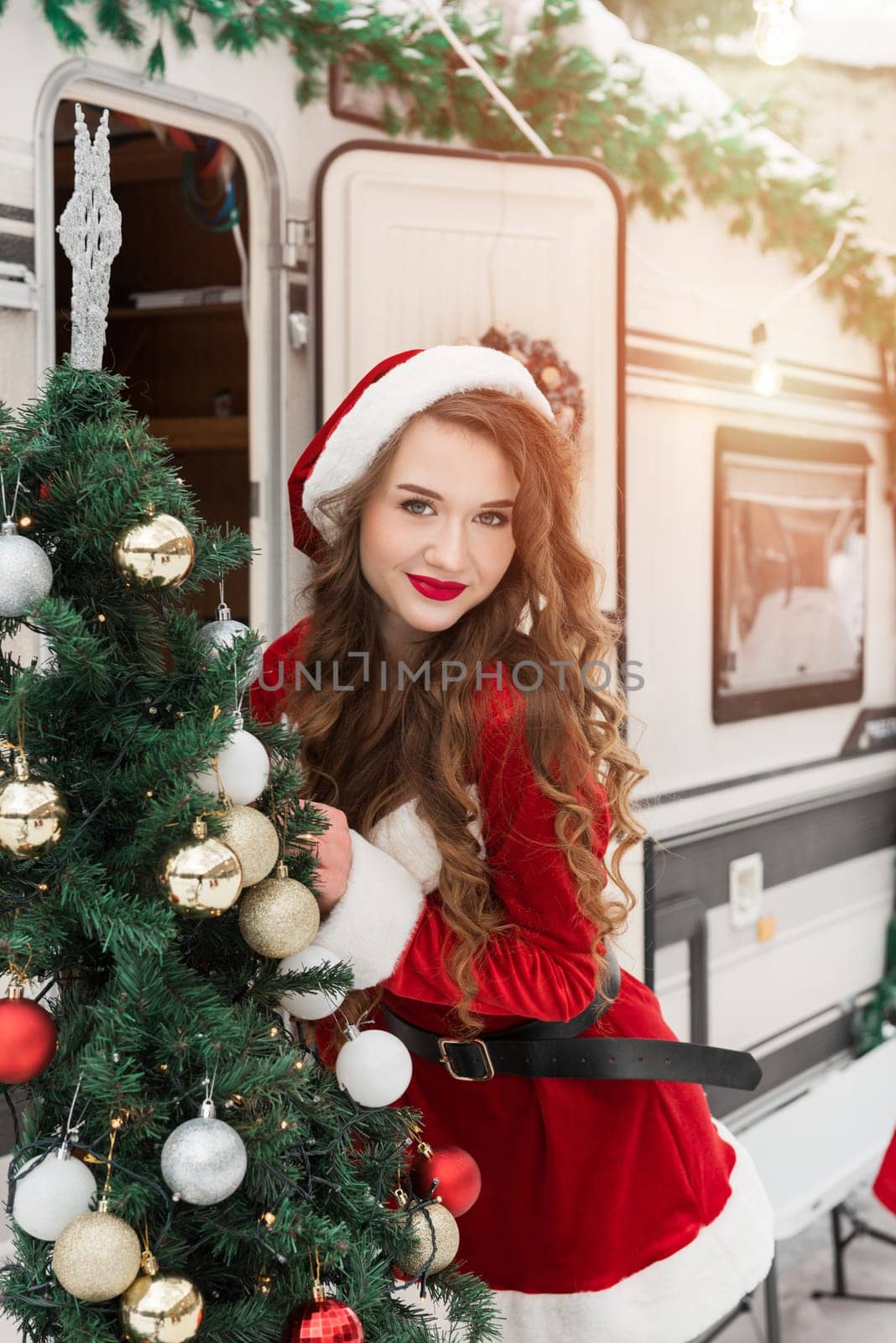 Young woman in santa costume decorates the Christmas tree at winter campsite getting ready for the new year. New year celebration concept