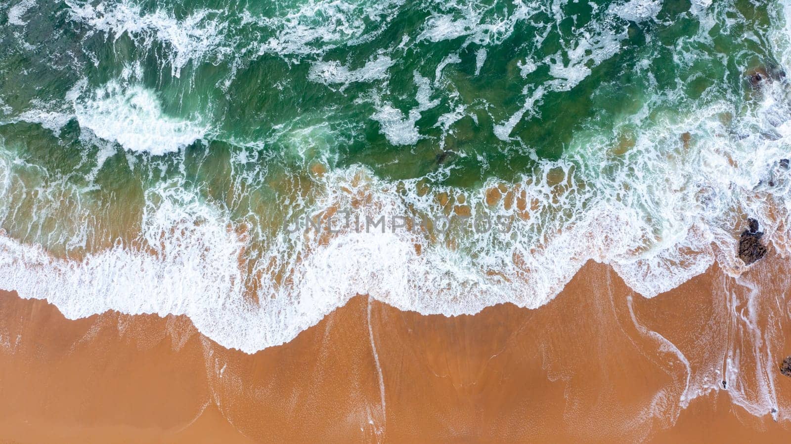 Drone view of beautiful seamless footage while turquiose sea waves breaking on sandy coastline. Aerial shot of golden beach meeting deep blue ocean water and foamy waves