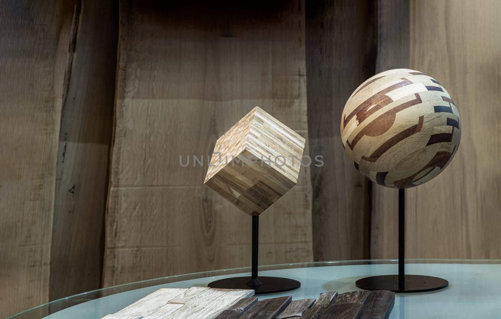 Bangkok,Thai - Apr 29, 2022 : The Wooden Craft Cube and the Wooden Craft Round Ball are made from the Pieces of Compound with the Small Wood, which are on the Glass Table Sheet with the Wooden Planks Wall Background. Fragment of the interior. Space for text, Selective focus.