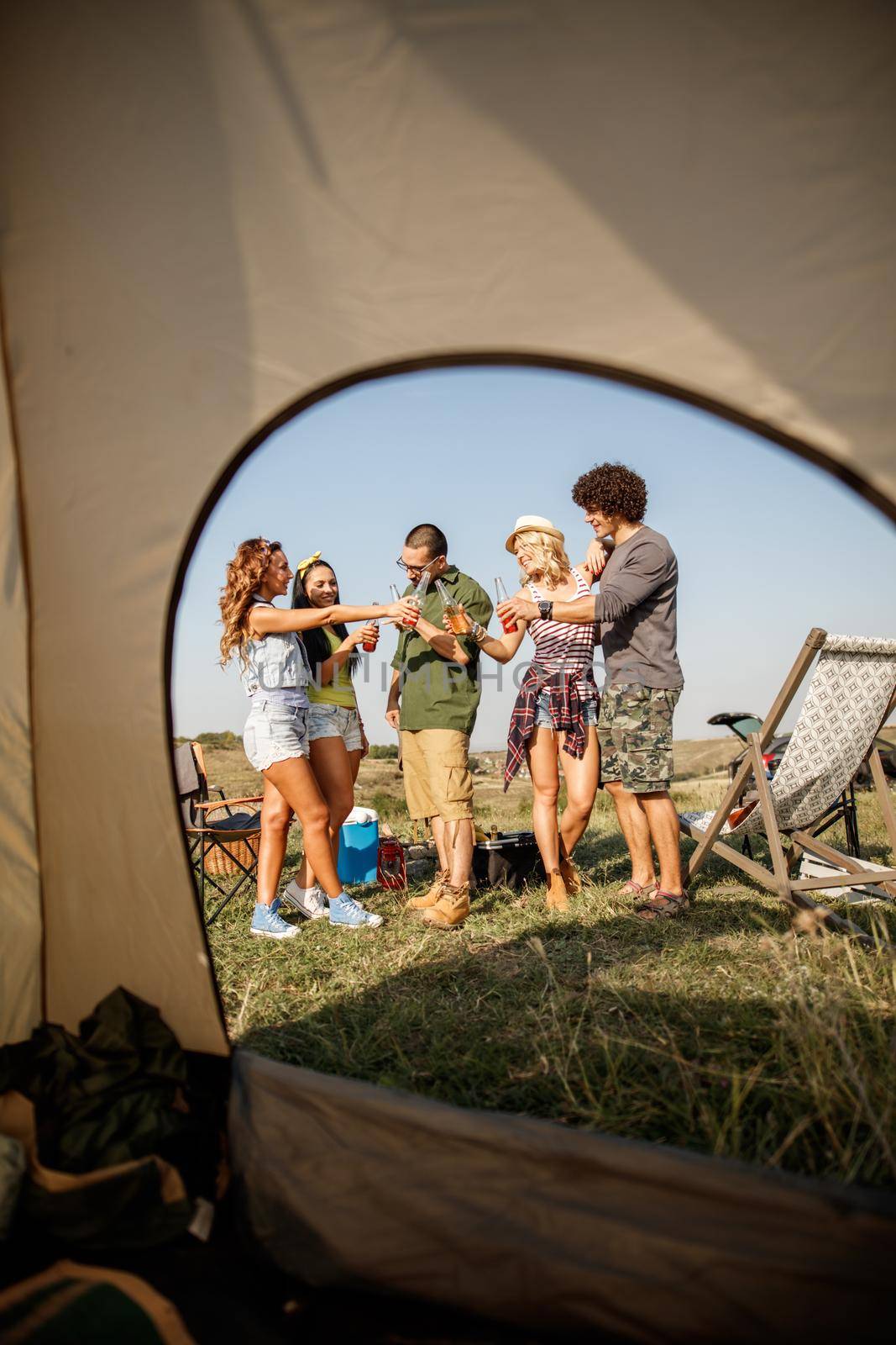 A group of cheerful friends sitting outside their tent at a festival.