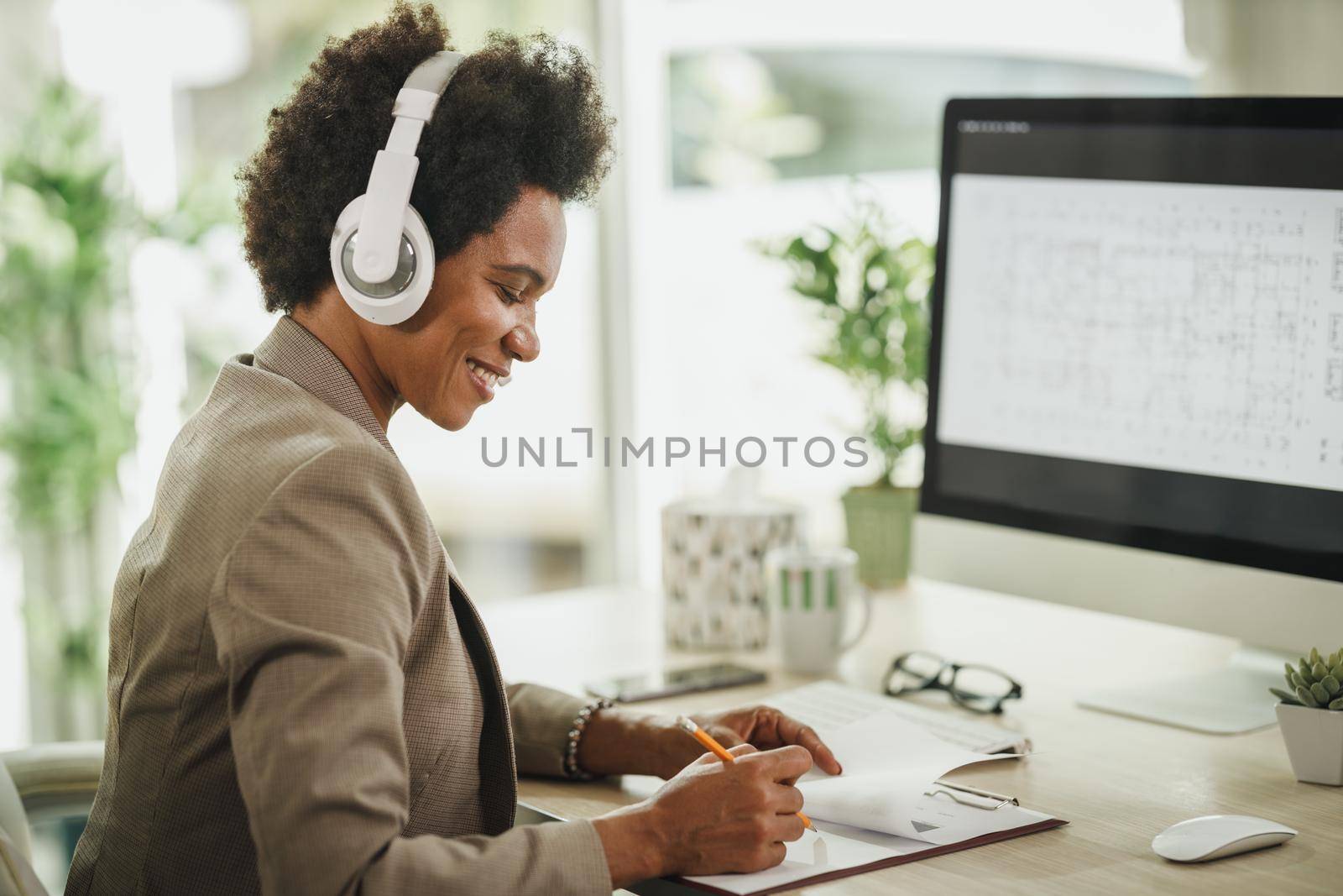 Shot of an African businesswoman wearing a headphones while working on her computer during corona virus pandemic.