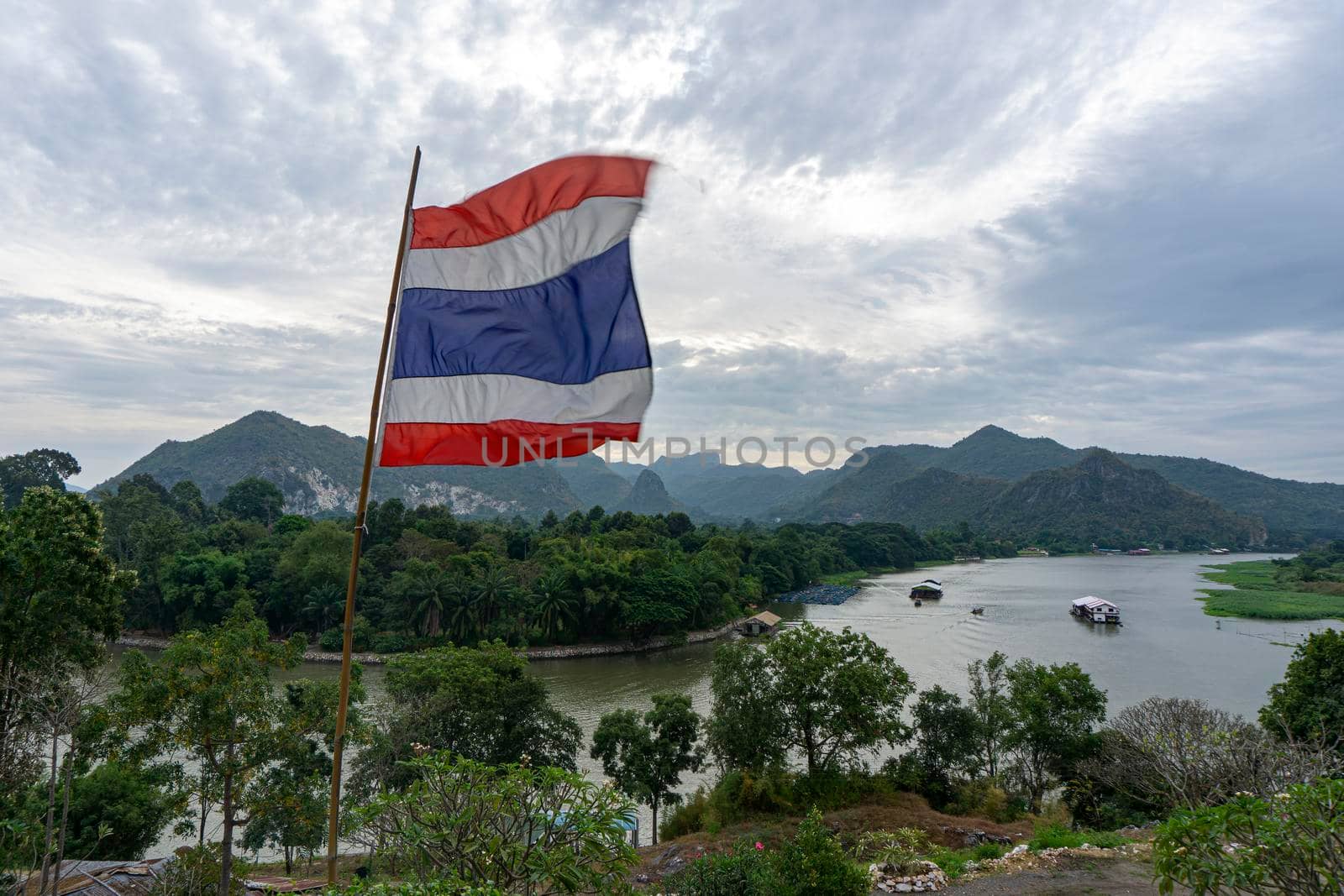 Thai flag blown from the wind, the background is the view of the River Kwai and the mountains of Kanchanaburi, Thailand