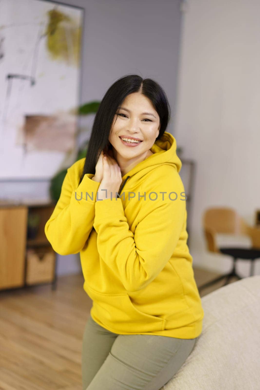 Mature Asian woman is captured in her home, enjoying the happy moments of life through the lens of lifestyle biohacking. She is surrounded by greenery and natural sunlight, as she focuses on wellness, fitness, and mental health by LipikStockMedia