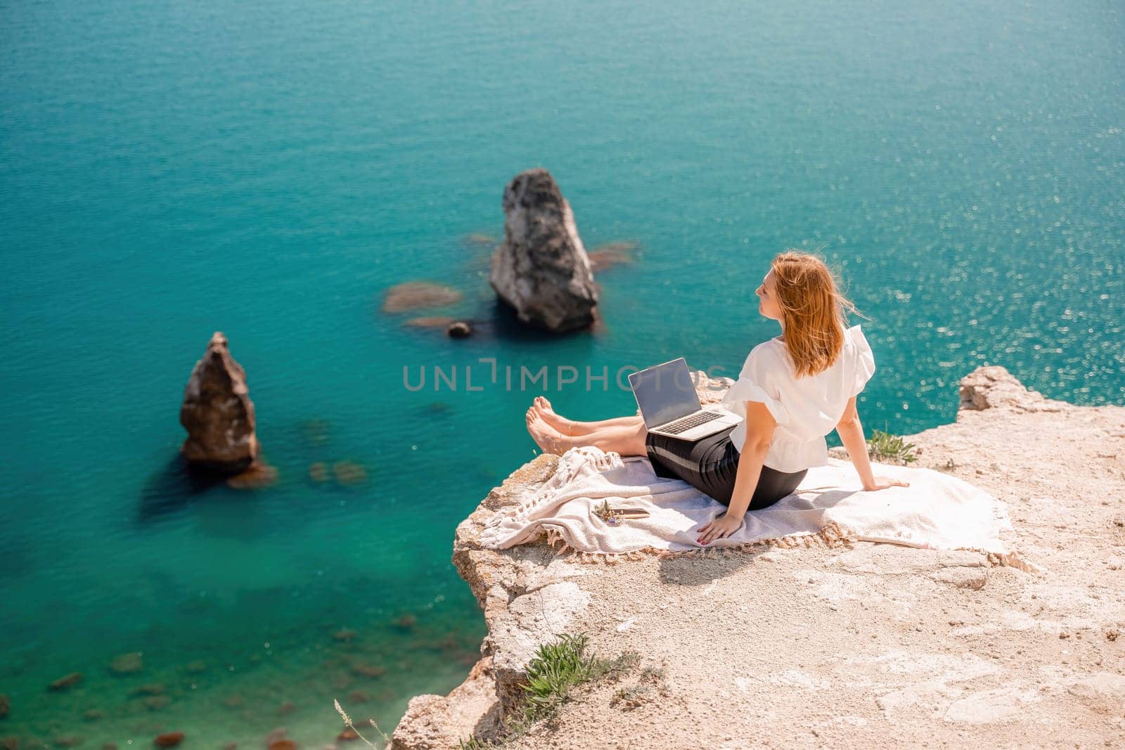 Freelance women sea working on the computer. Good looking middle aged woman typing on a laptop keyboard outdoors with a beautiful sea view. The concept of remote work. by Matiunina