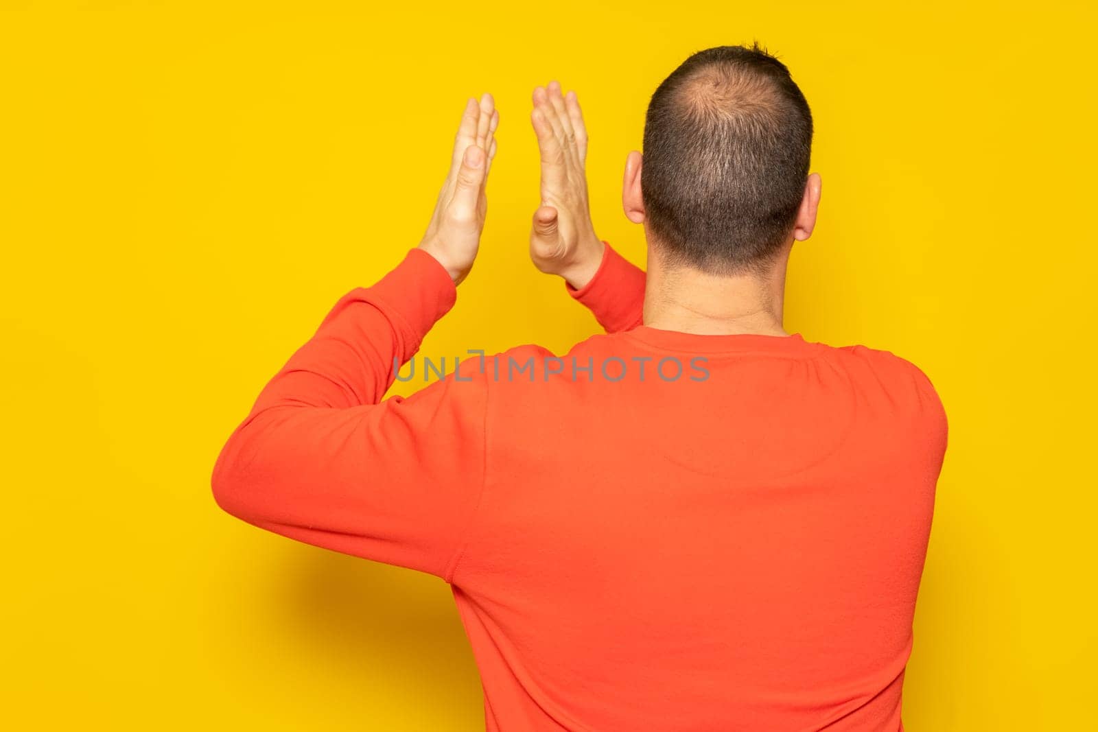 Half-bald man energetically clapping his back, he is excited about the spectacle he has just witnessed. Isolated on yellow background