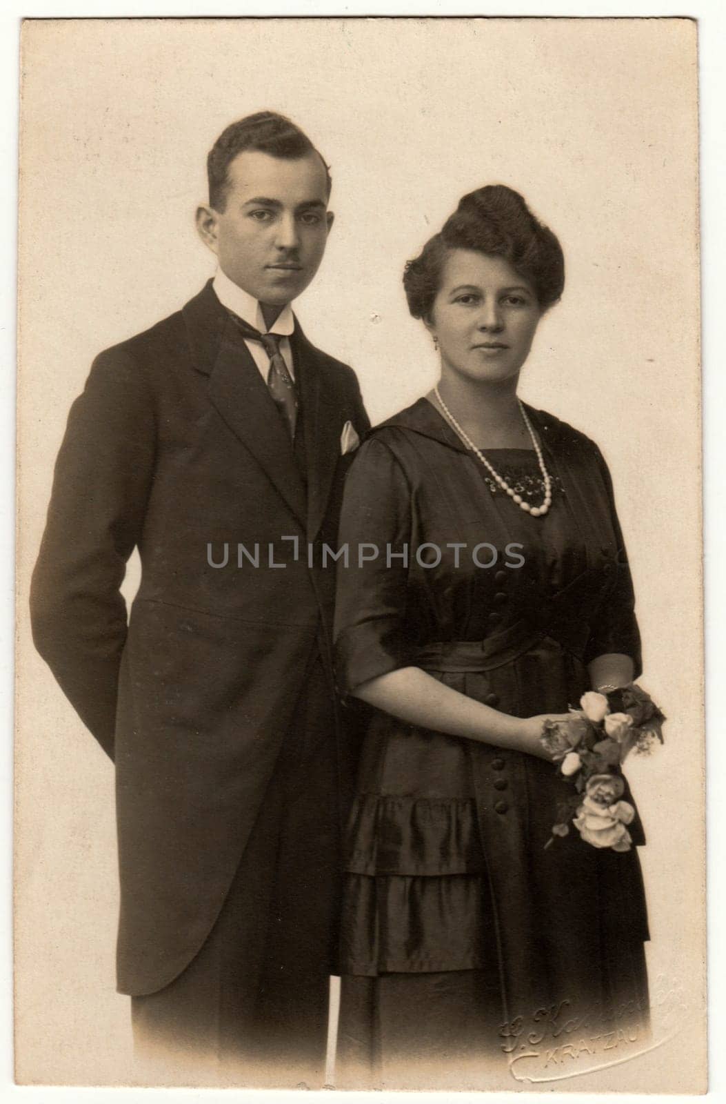 Vintage photo shows a young couple wears black clothes. Woman holds flowers. Retro black and white photography. Circa 1920s by roman_nerud