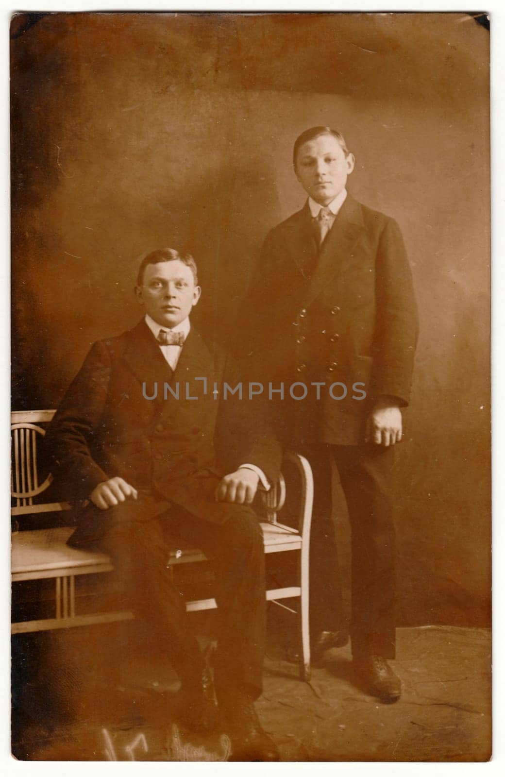 Vintage photo shows young boys brothers pose in a photography studio. Retro black and white photography with sepia effect. Circa 1910s. by roman_nerud