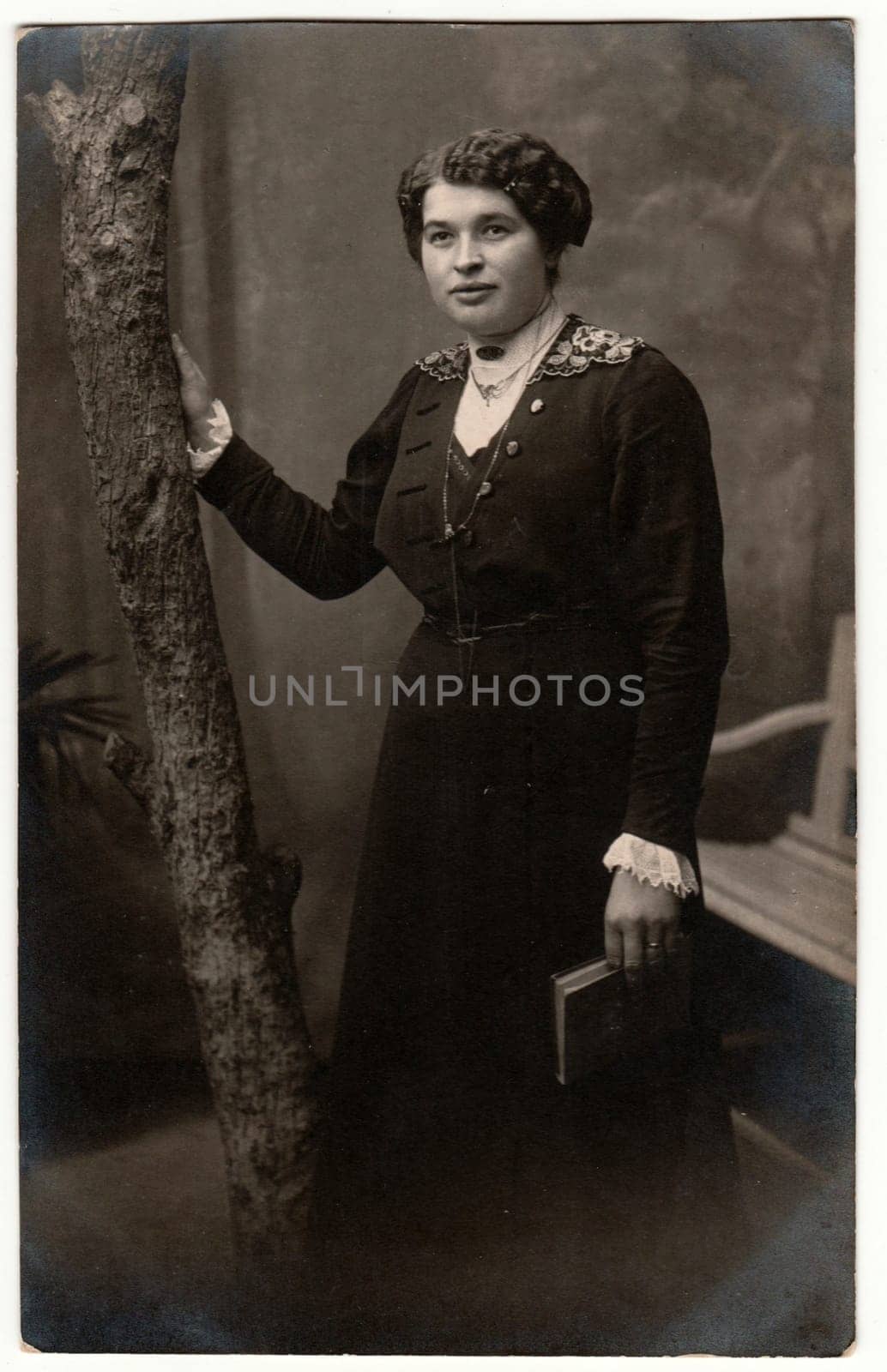 Vintage photo shows woman with short hair. Woman holds book. Retro black and white studio photography with sepia effect. Circa 1920s. by roman_nerud