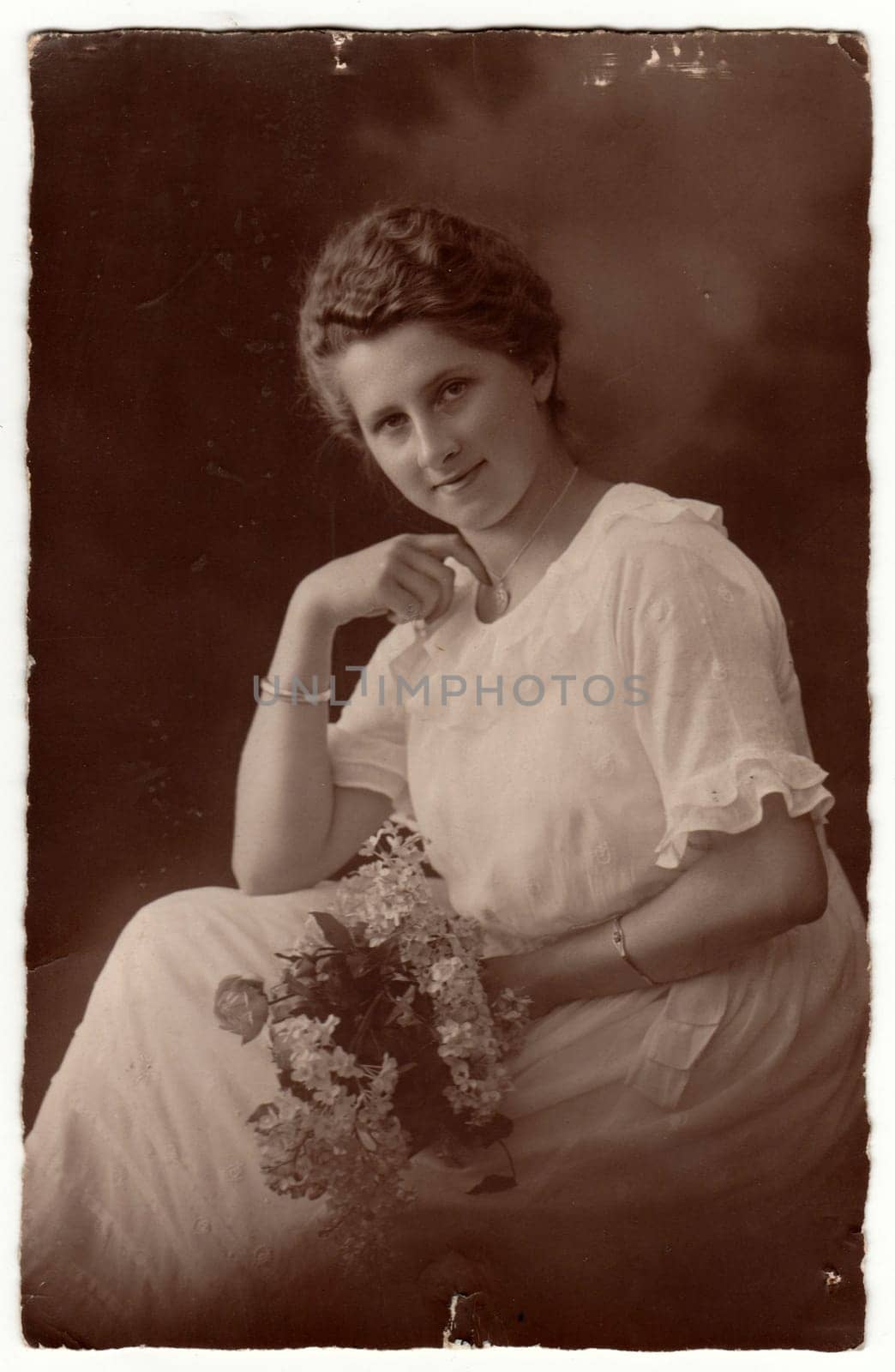 GERMANY - CIRCA 1920s: Vintage photo shows woman with short hair. Woman wears white dress and holds bouquet - bunch of flowers. Retro black and white studio photography with sepia effect. Circa 1920s