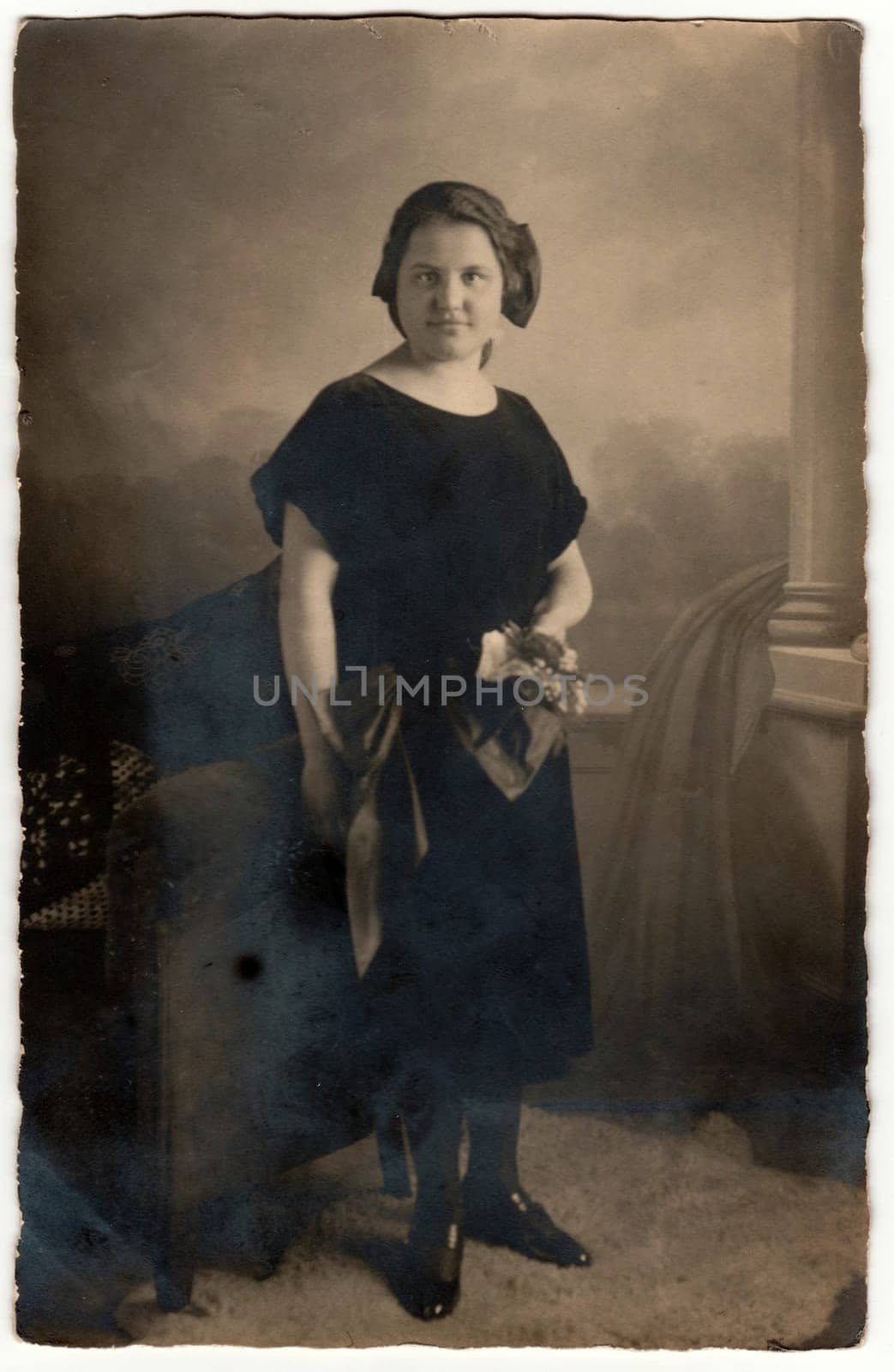 GERMANY - CIRCA 1920s: Vintage photo shows woman with short hair. Woman wears black dress and holds bouquet - bunch of flowers. Retro black and white studio photography with sepia effect. Circa 1920s.
