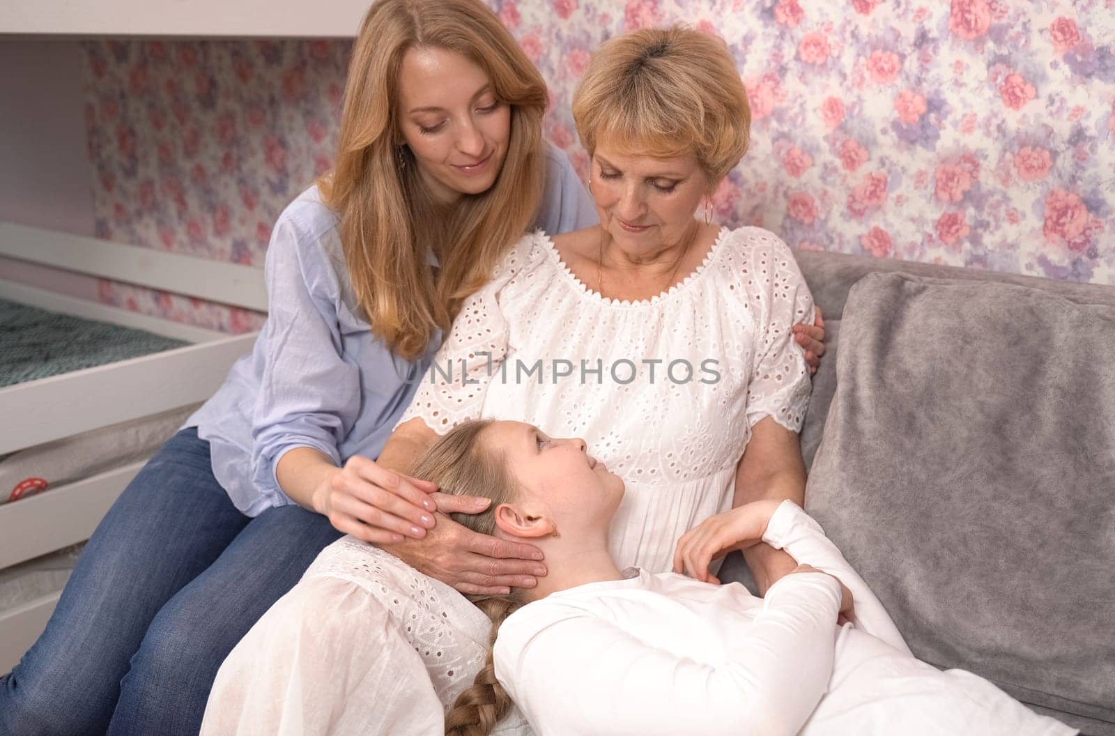 The granddaughter lies on her grandmother's legs, look smiling at her mother and grandmother. A happy family.