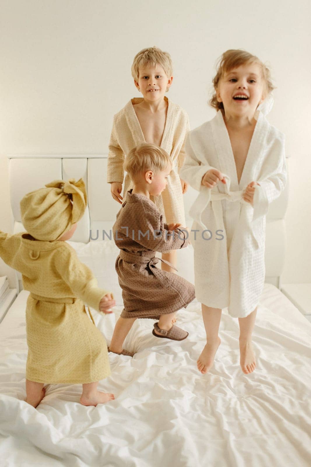 Joyful children in bathrobes play on the bed - they jump.