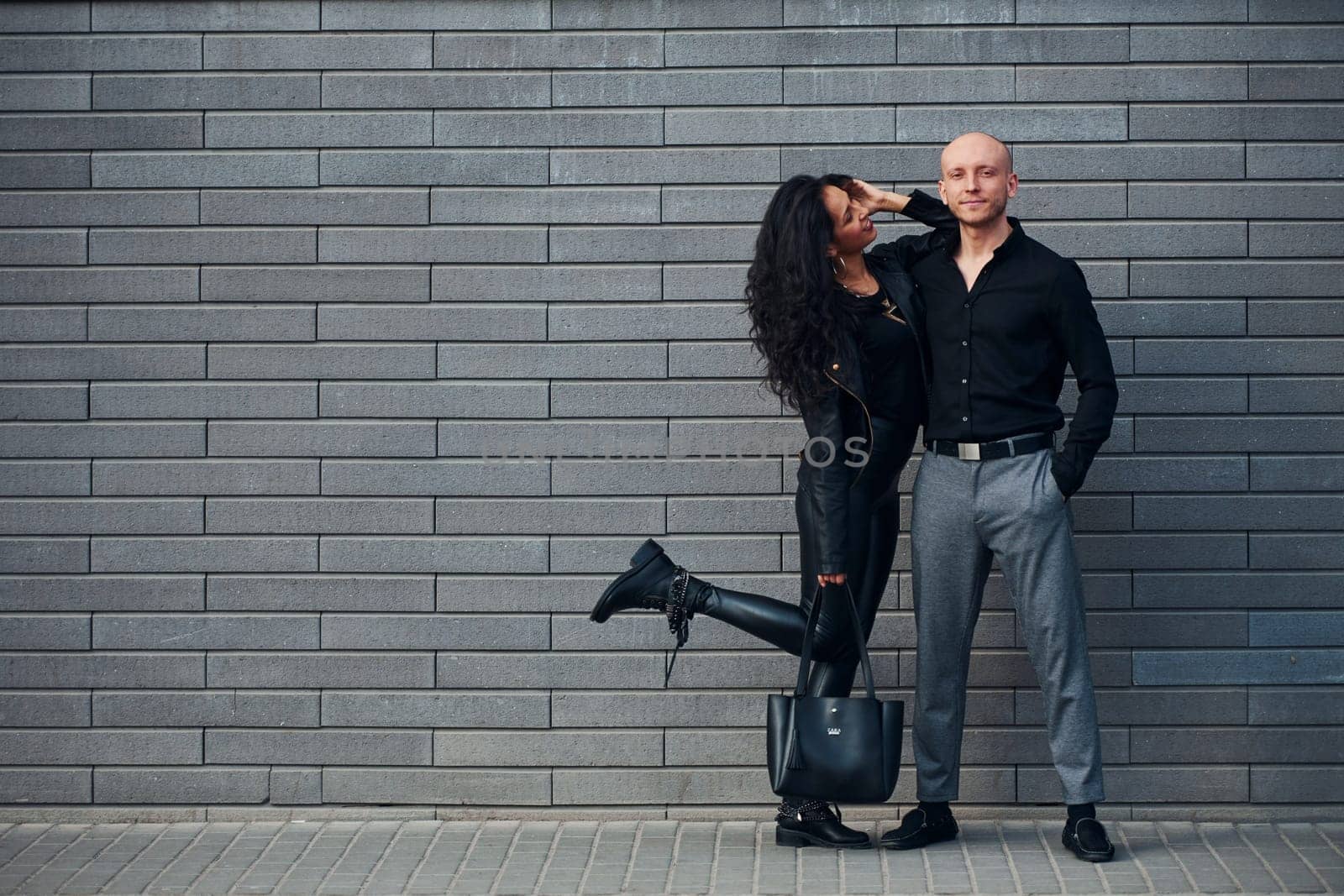 Beautiful couple in black clothes together against wall outdoors.