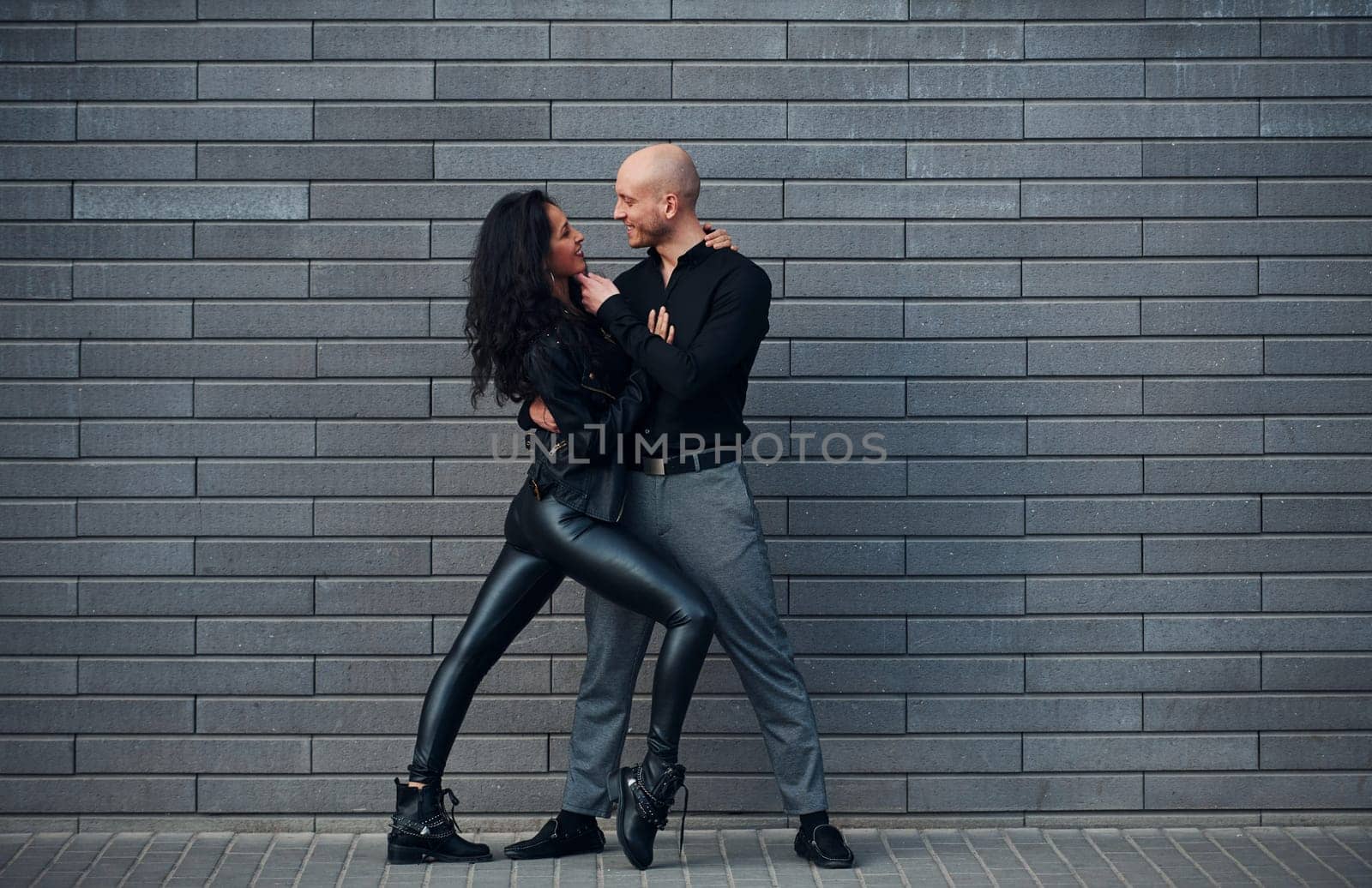 Beautiful couple in black clothes dancing together against wall outdoors by Standret