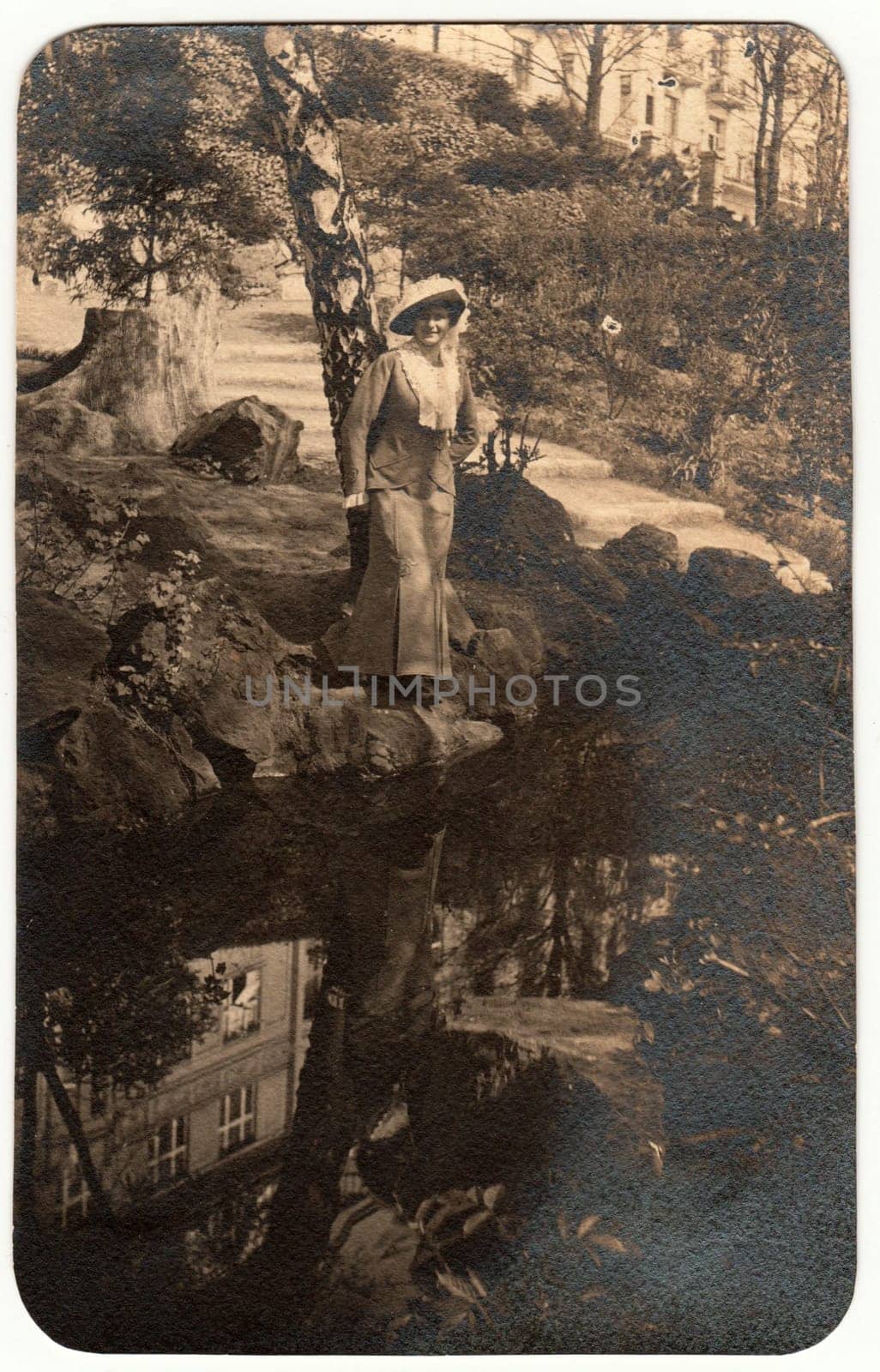 THE CZECHOSLOVAK REPUBLIC - CIRCA 1930s: Vintage photo shows woman wears an elegant dress and feather hat. The woman poses outdoors at the bank of river. Retro black and white photography. Circa 1960s.