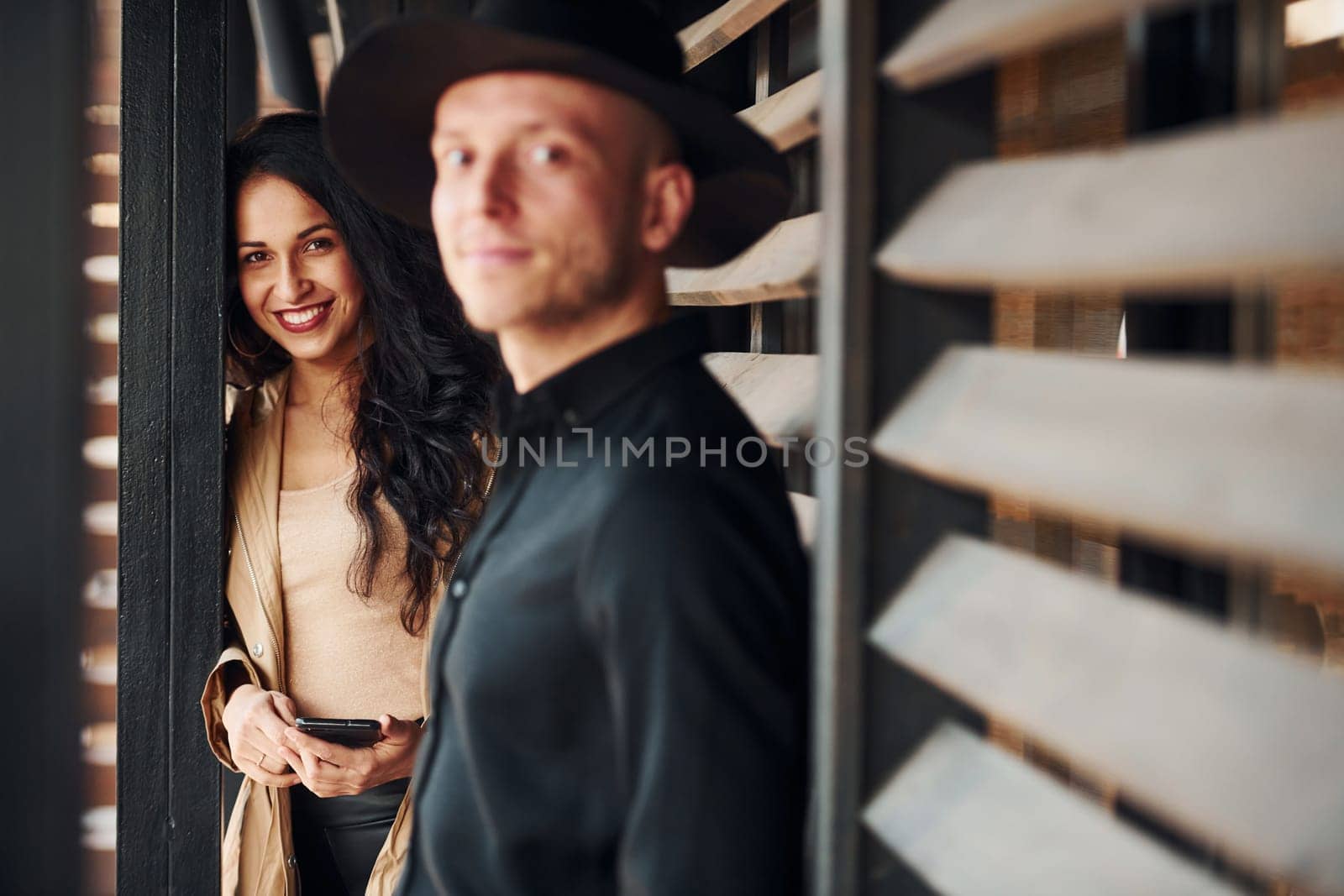 Woman with black curly hair and her man standing together near wooden windows by Standret
