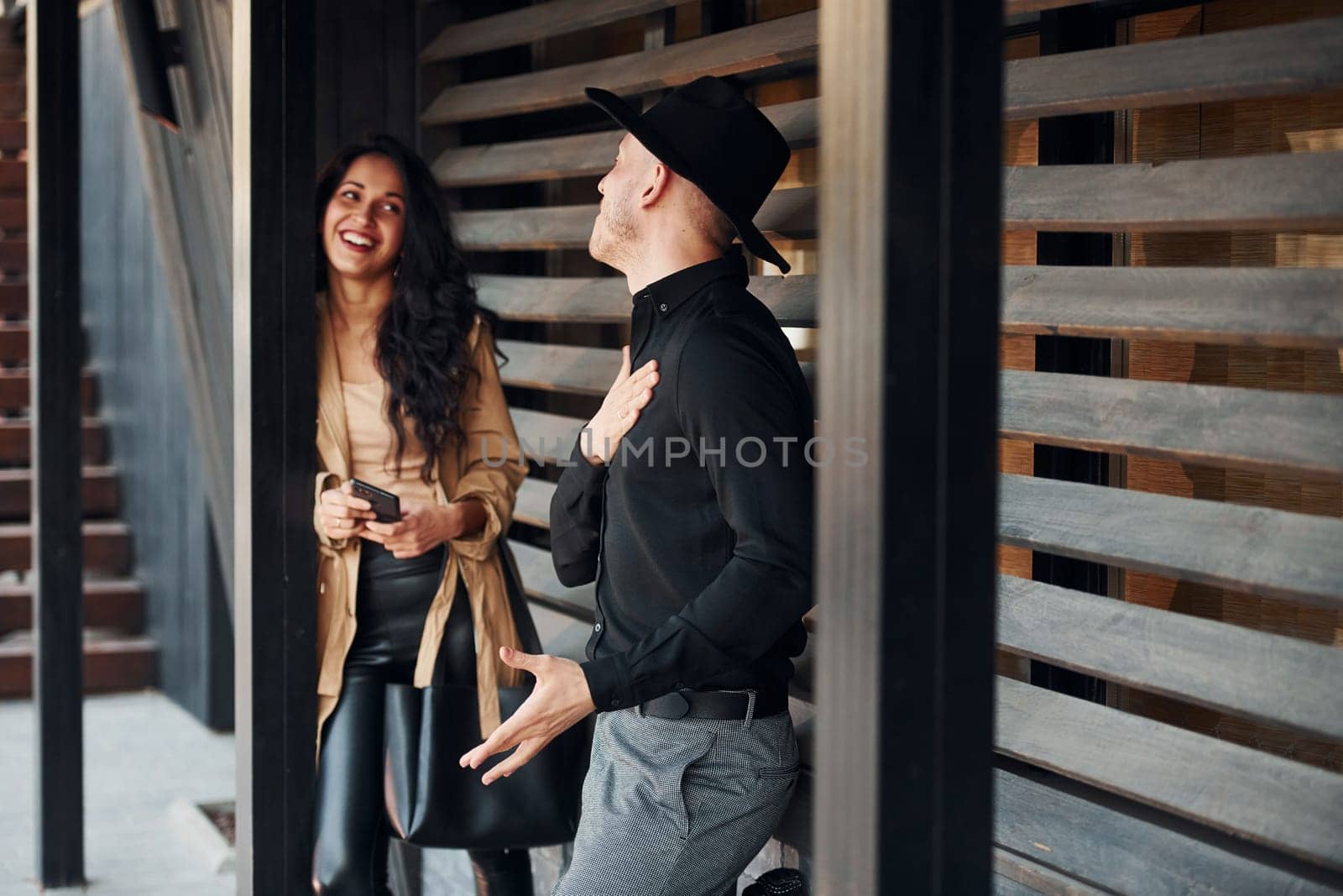 Woman with black curly hair and her man standing together near wooden windows.