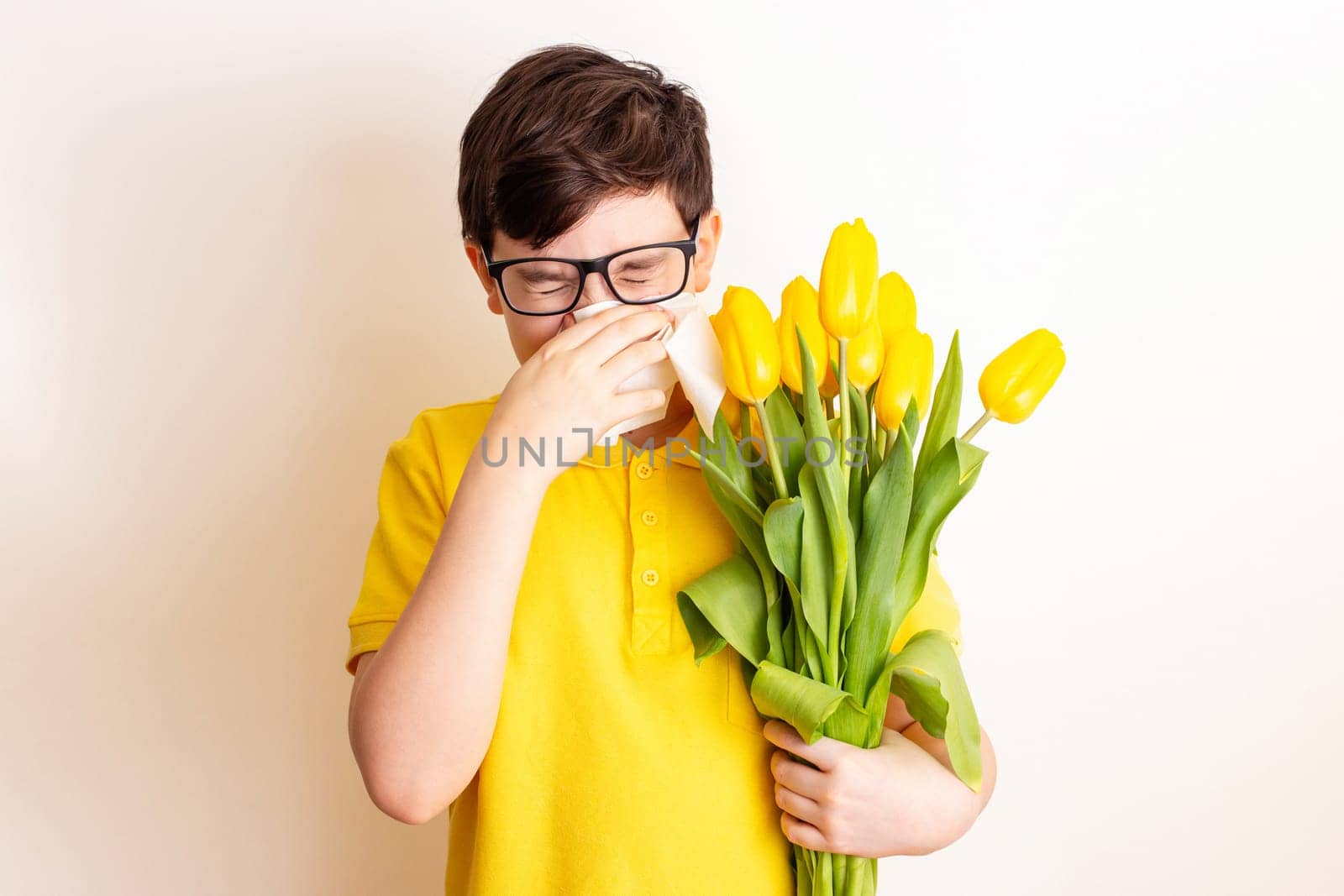 a brunette boy , dressed in a yellow T-shirt, holds a bouquet of yellow tulips and covered his nose with a paper napkin and sneezes, on a white background. To close up.