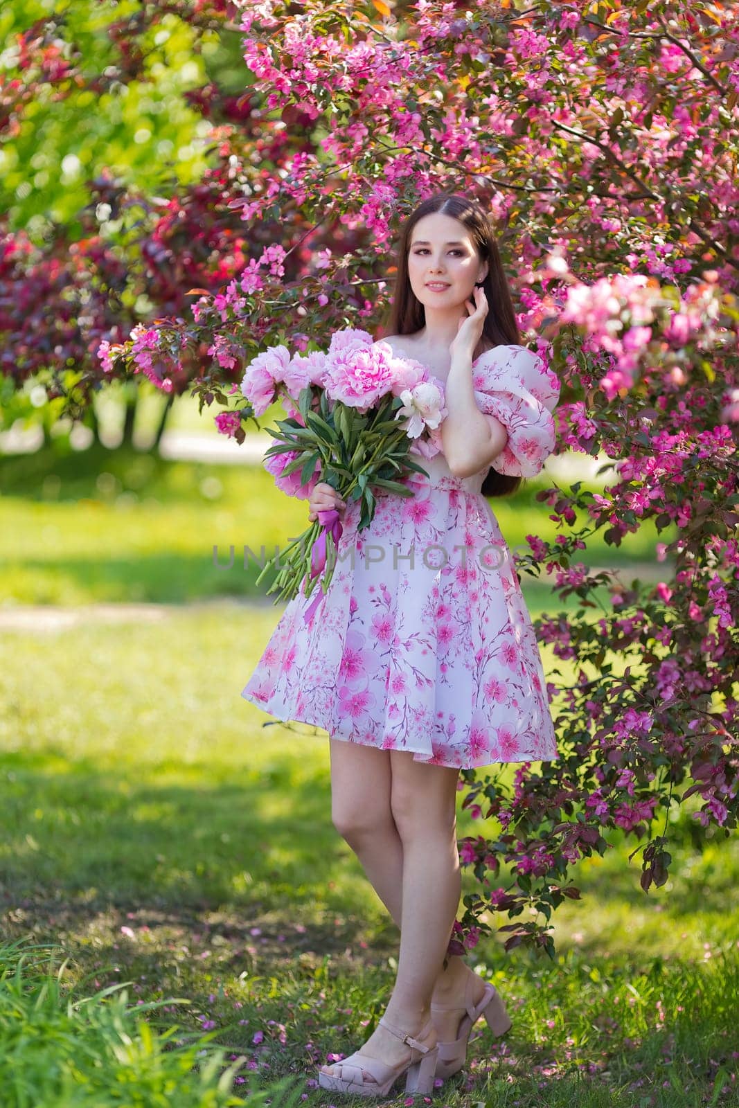 girl, stands with a bouquet of peonies, near pink flowering trees by Zakharova