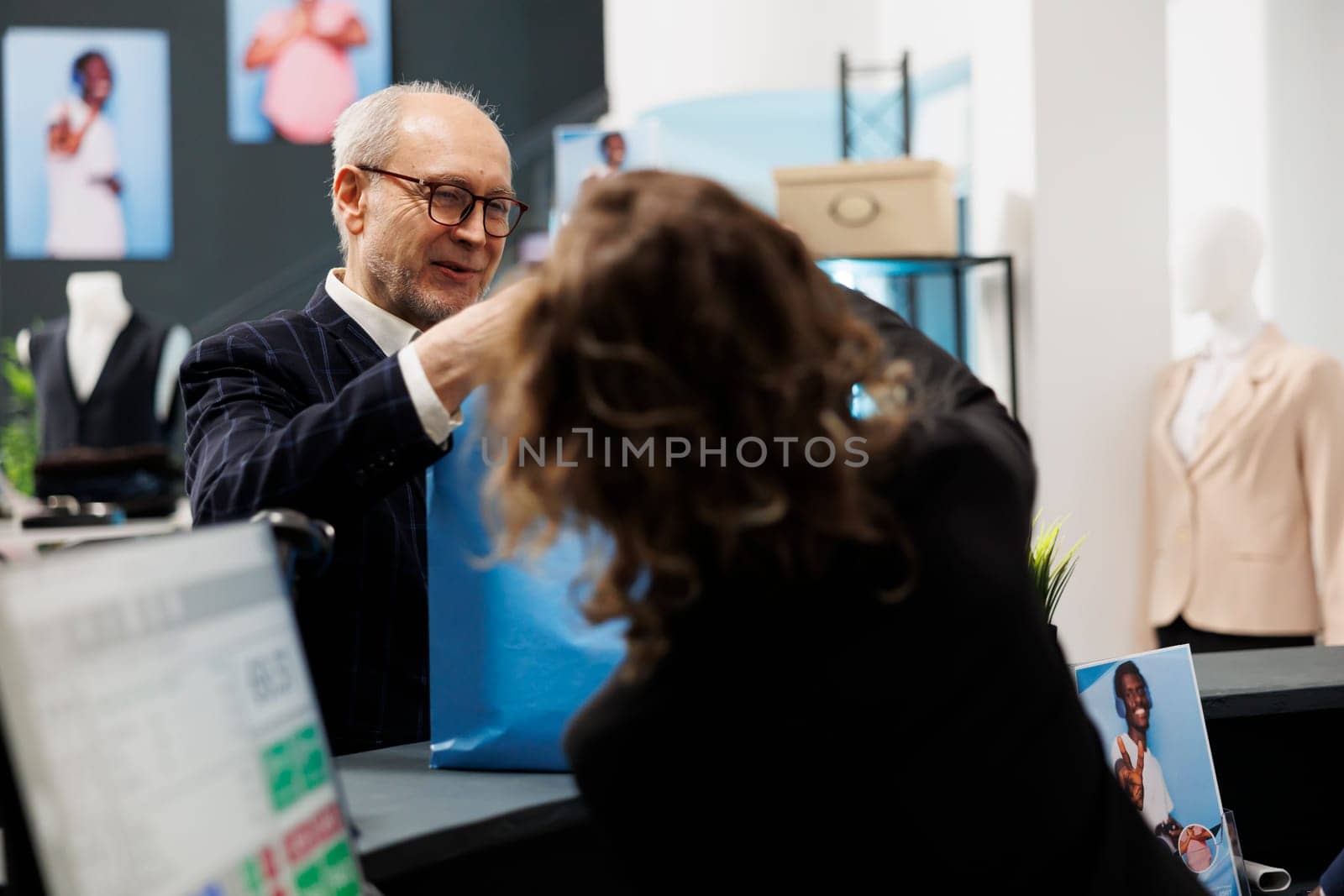 Old client taking shopping bag from boutique employee, after buying fashionable clothes in shopping centre. Senior shopper paying for stylish merchandise during commercial activity