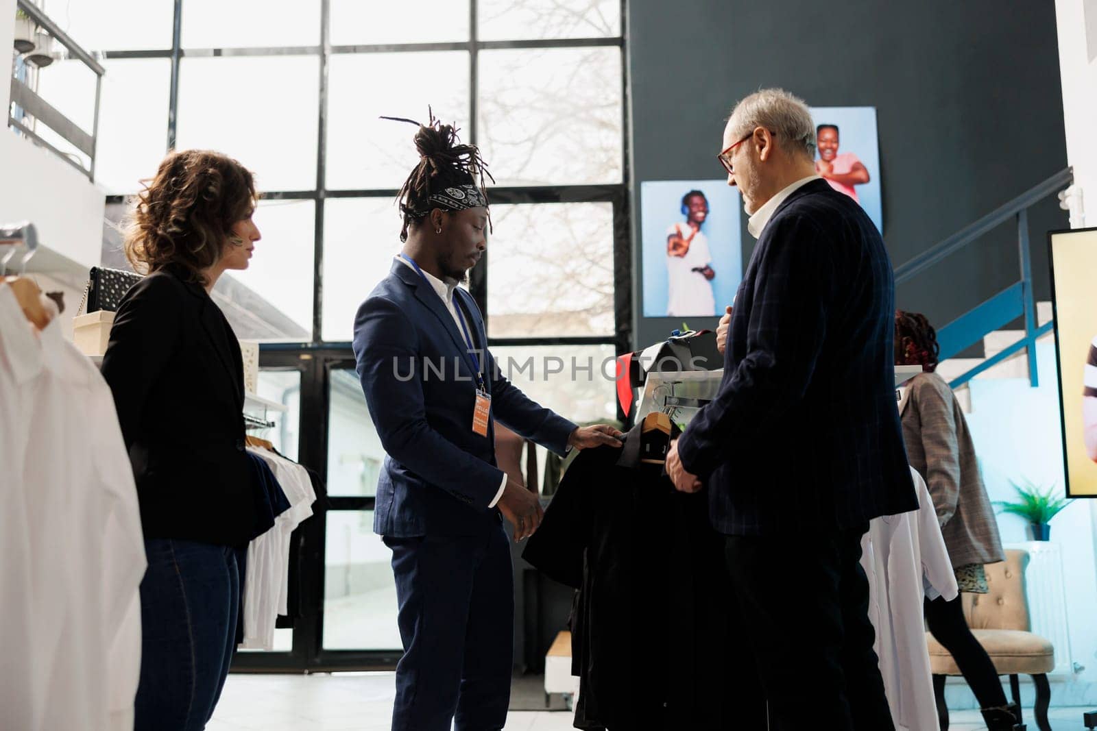 Elderly customer wanting to buy formal suit, asking showroom employee for help to choose the right clothes. Senior man buying fashionable merchandise and stylish accessories in clothing store