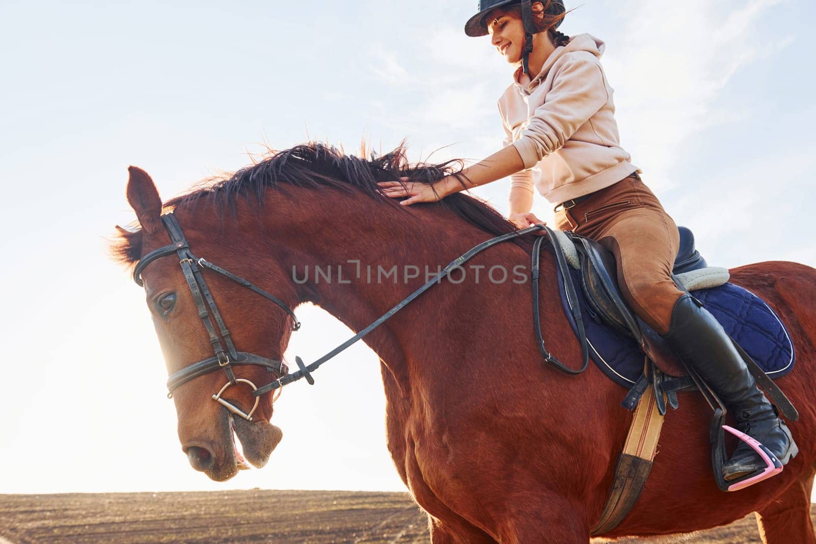 Young woman in protective hat with her horse in agriculture field at sunny daytime by Standret