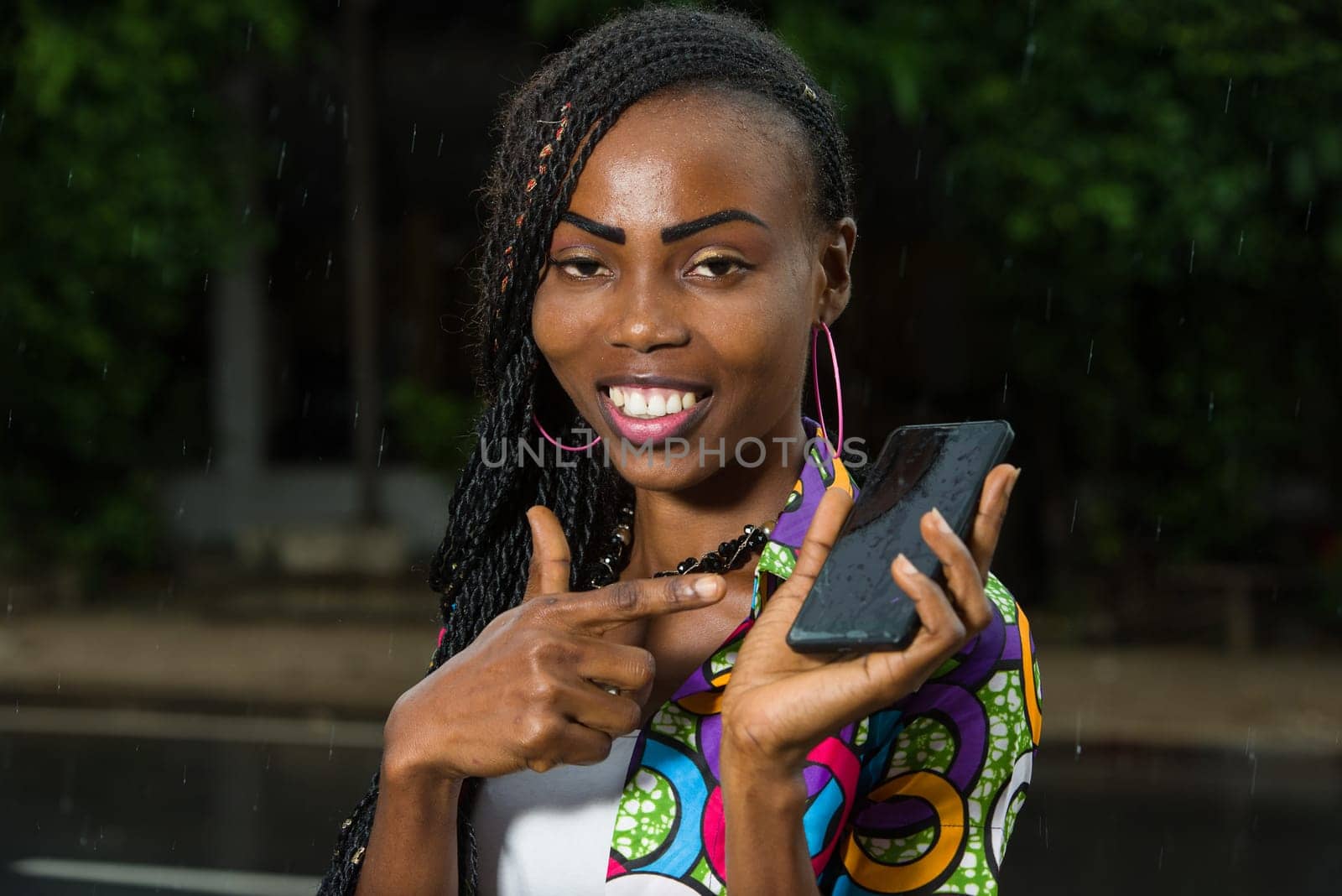 young girl under a light rain show mobile phone smiling.