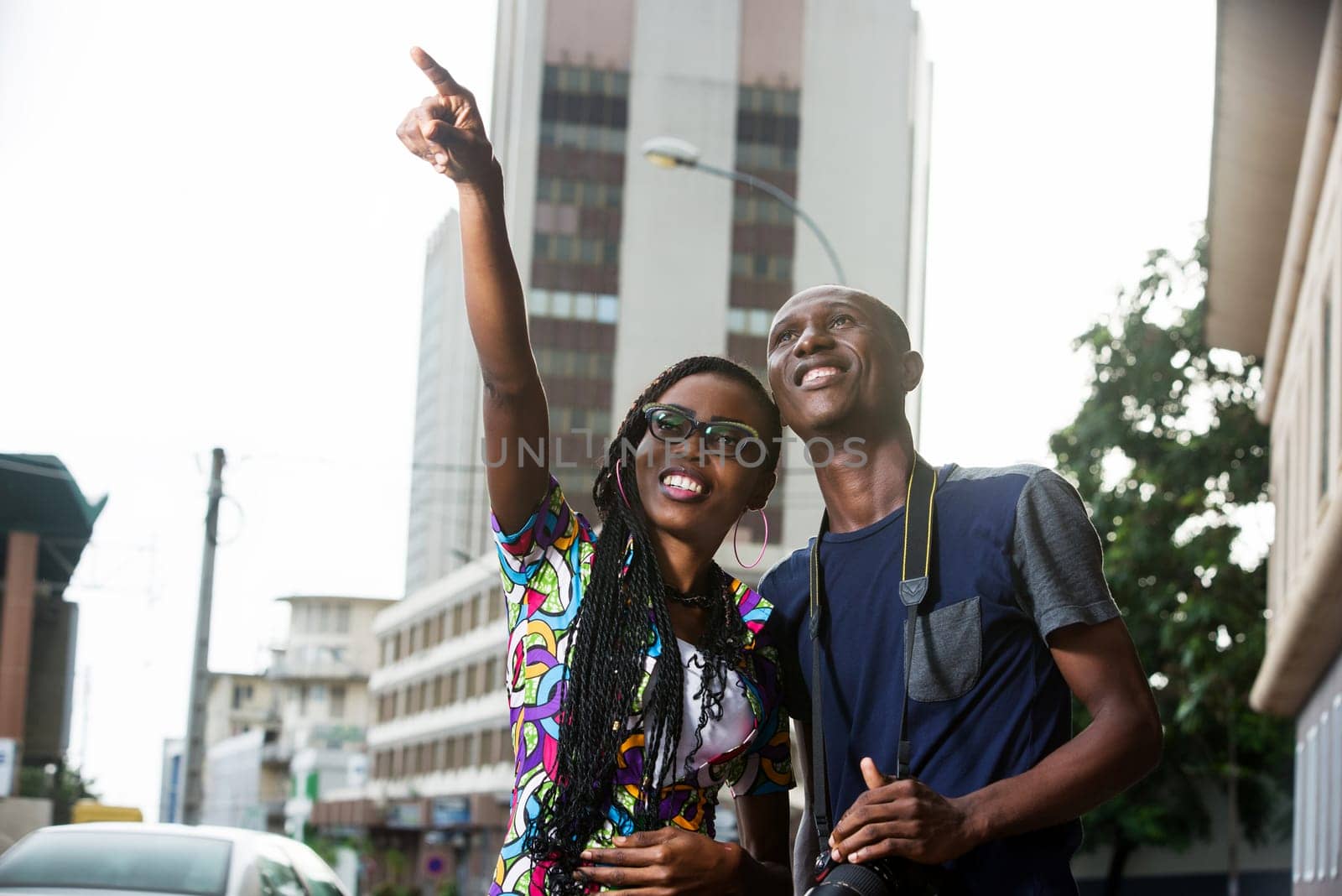 young girl standing in eyeglasses showing something to her smiling photographer friend.