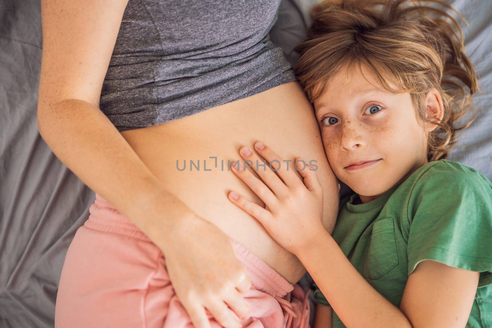 Young beautiful pregnant woman and eldest son. The cute boy leaned his ear against his mother's belly. Expecting a baby in the family concept. Preparing an older child for a younger one.