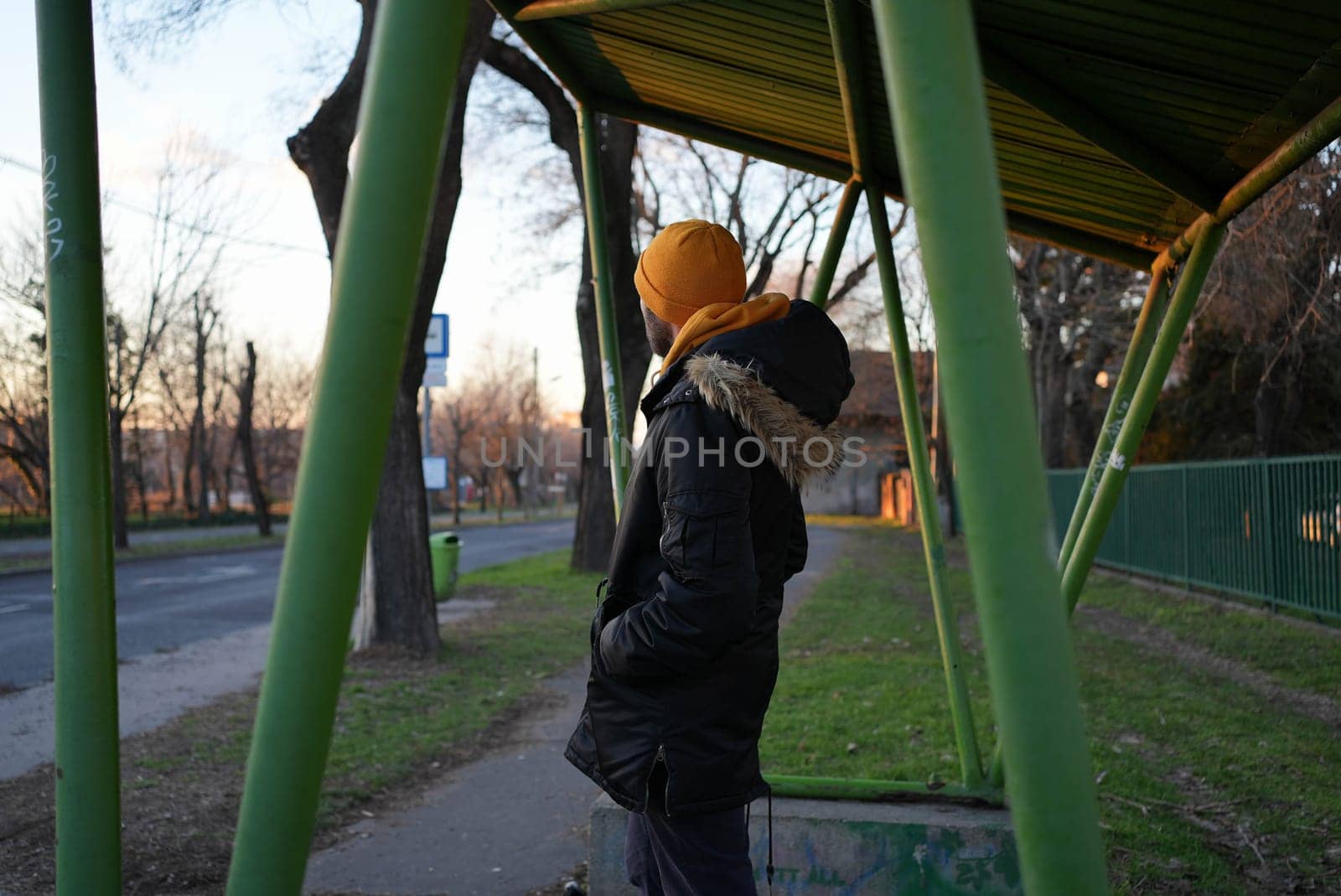 Guy in winter coat waiting for bus at a suburban bus stop. High quality photo